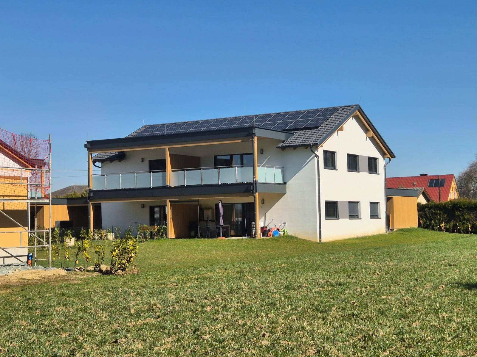 Neues Einfamilienhaus mit Photovoltaikanlage, Balkon und Terrasse, umgeben von einer Grünfläche.