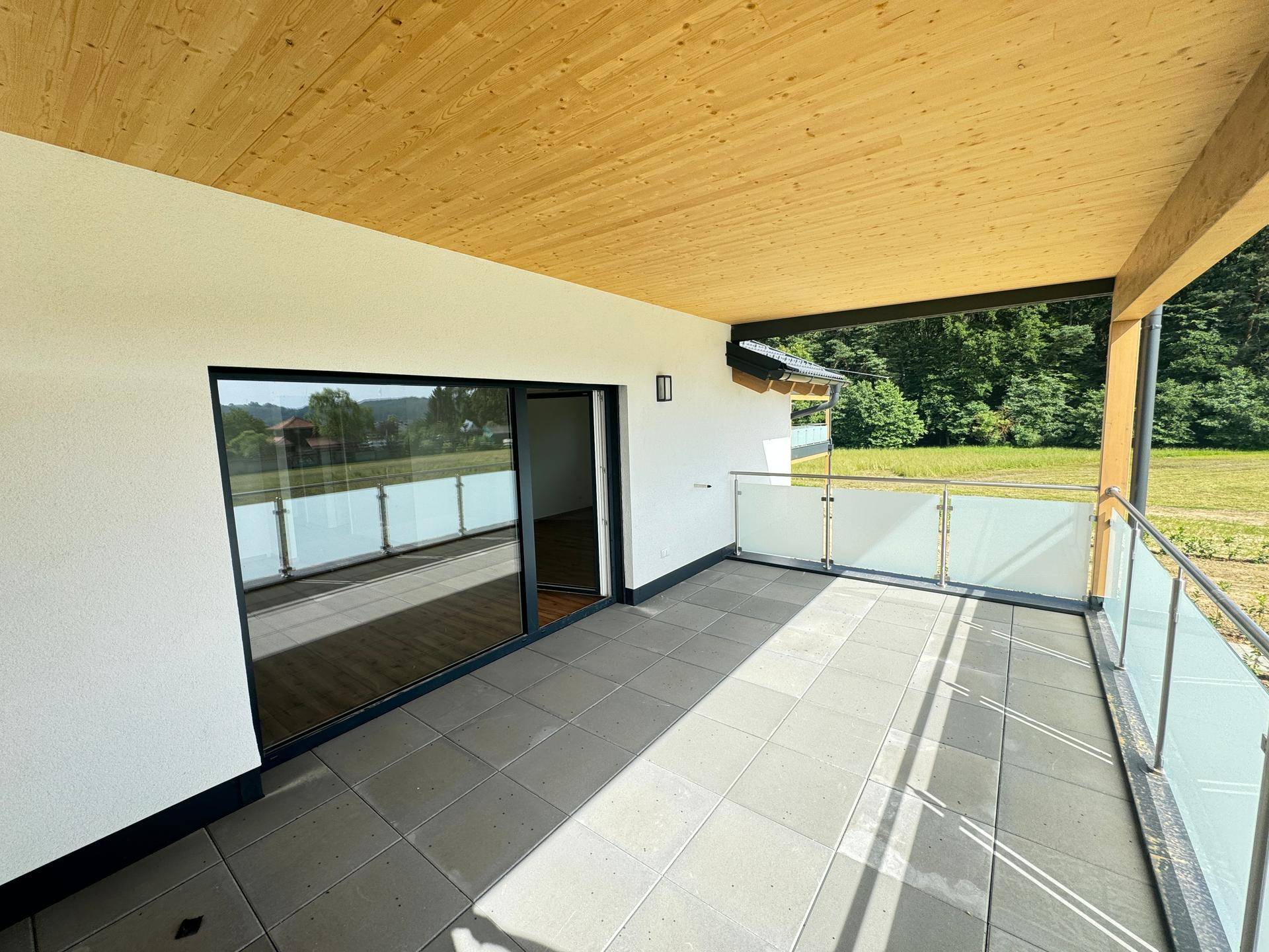 Geräumiger überdachter Balkon mit Fliesenboden und Blick auf die grüne Umgebung.