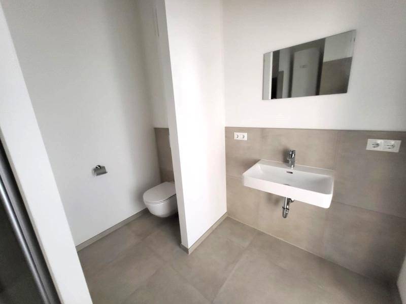 Modernes Badezimmer mit Wand-WC, Einzelwaschbecken und hellen Fliesen an Wänden und Boden.