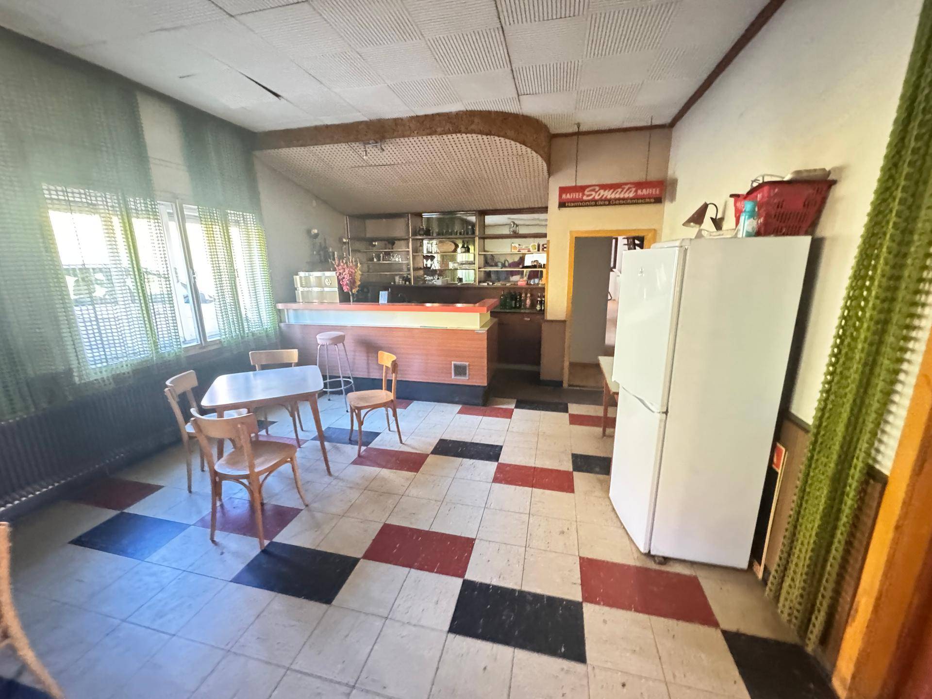 Geräumiger Wohn- und Essbereich mit Bar, kariertem Fliesenboden und großen Fenstern.