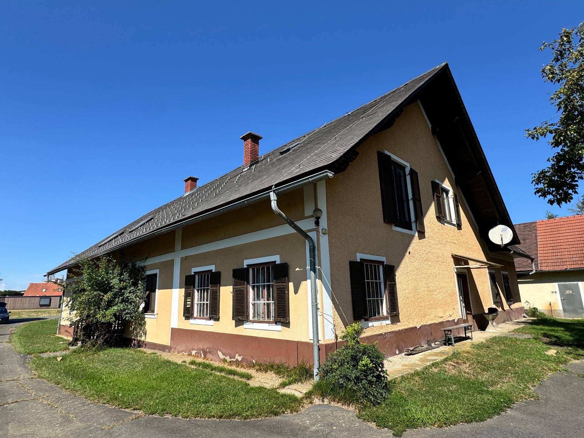 Traditionelles Haus mit gelber Fassade, braunen Fensterläden und Satteldach in ländlicher Umgebung.