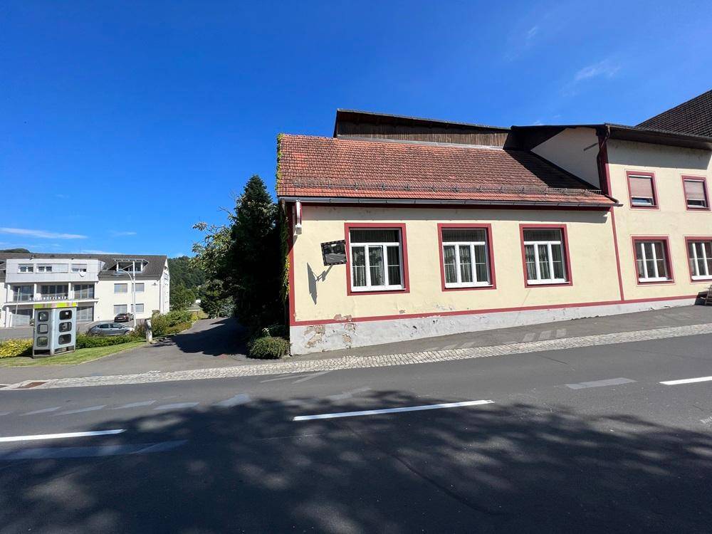 Seitenansicht des beigen Gebäudeteils mit grüner Bepflanzung und Blick auf die Umgebung.