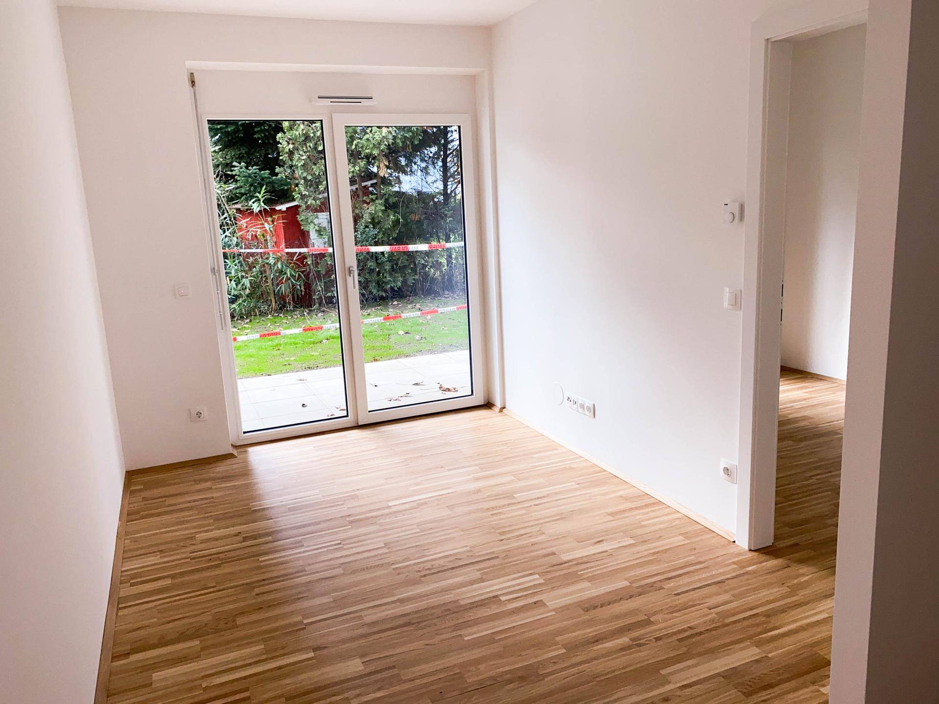 Heller Wohnraum mit Parkettboden und direktem Zugang zum Garten durch eine große Glastür.
