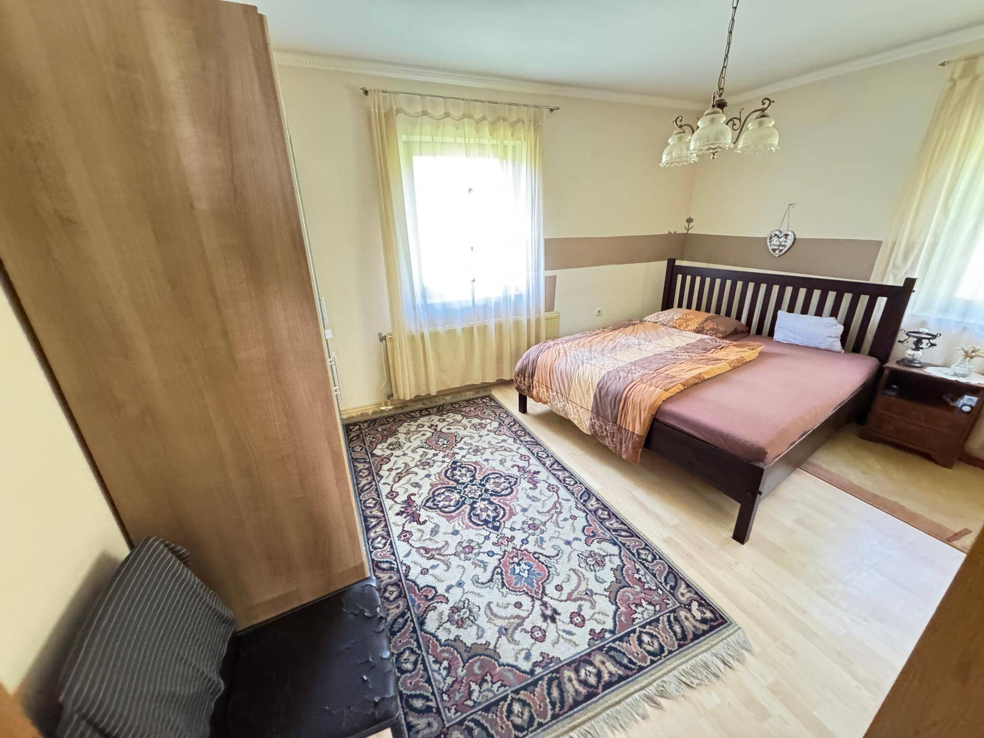 Schlafzimmer mit Doppelbett, Teppich und einem großen Fenster, das den Raum hell erscheinen lässt.