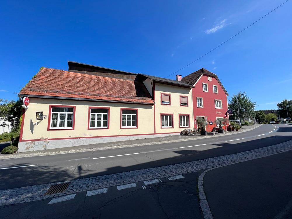 Seitenansicht des Gebäudes von der Straße, mit beiger Fassade und rotem Ziegeldach.