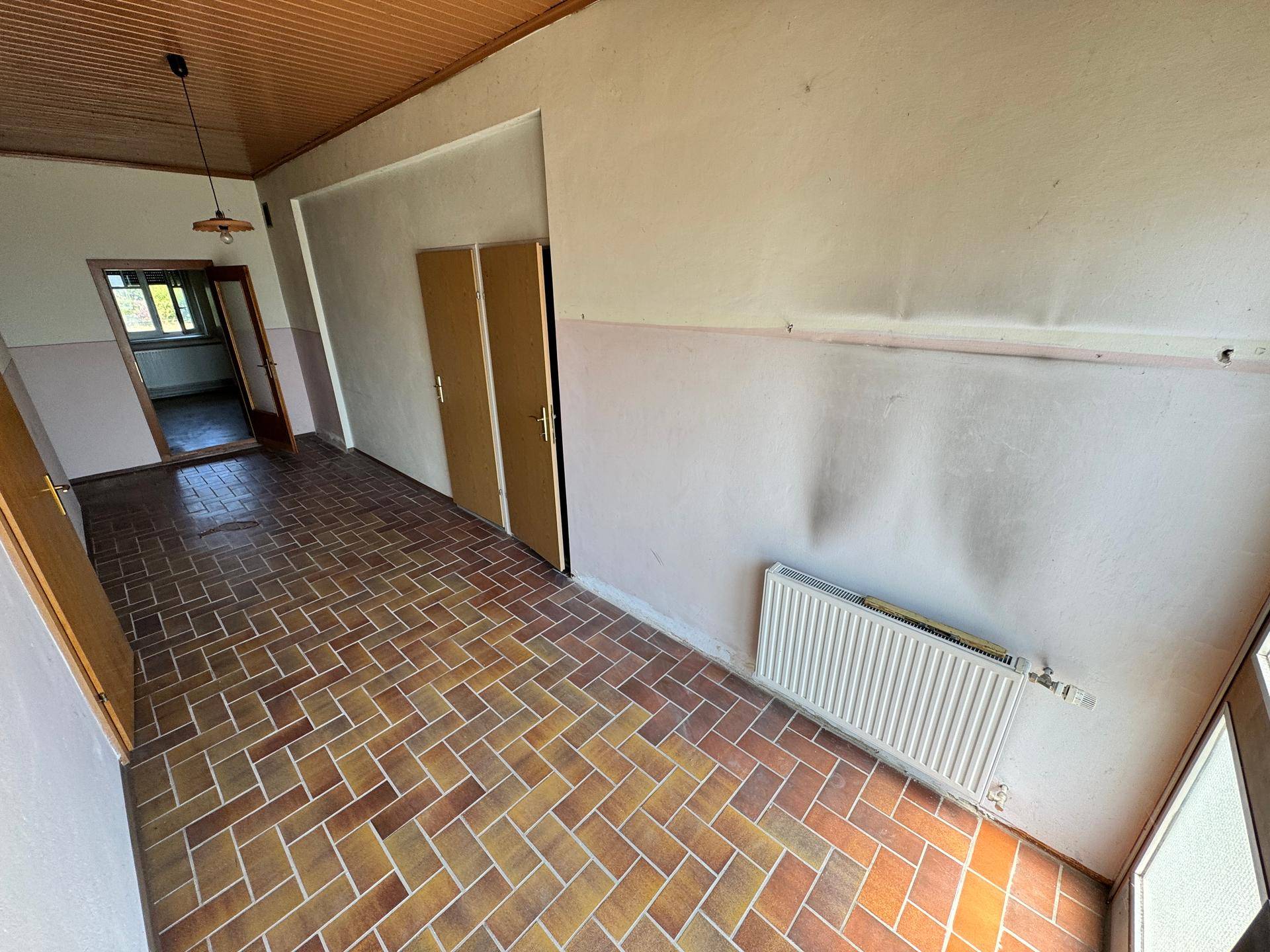 Flur mit Terrakotta-Fliesenboden, Holzdecke und Heizkörper.