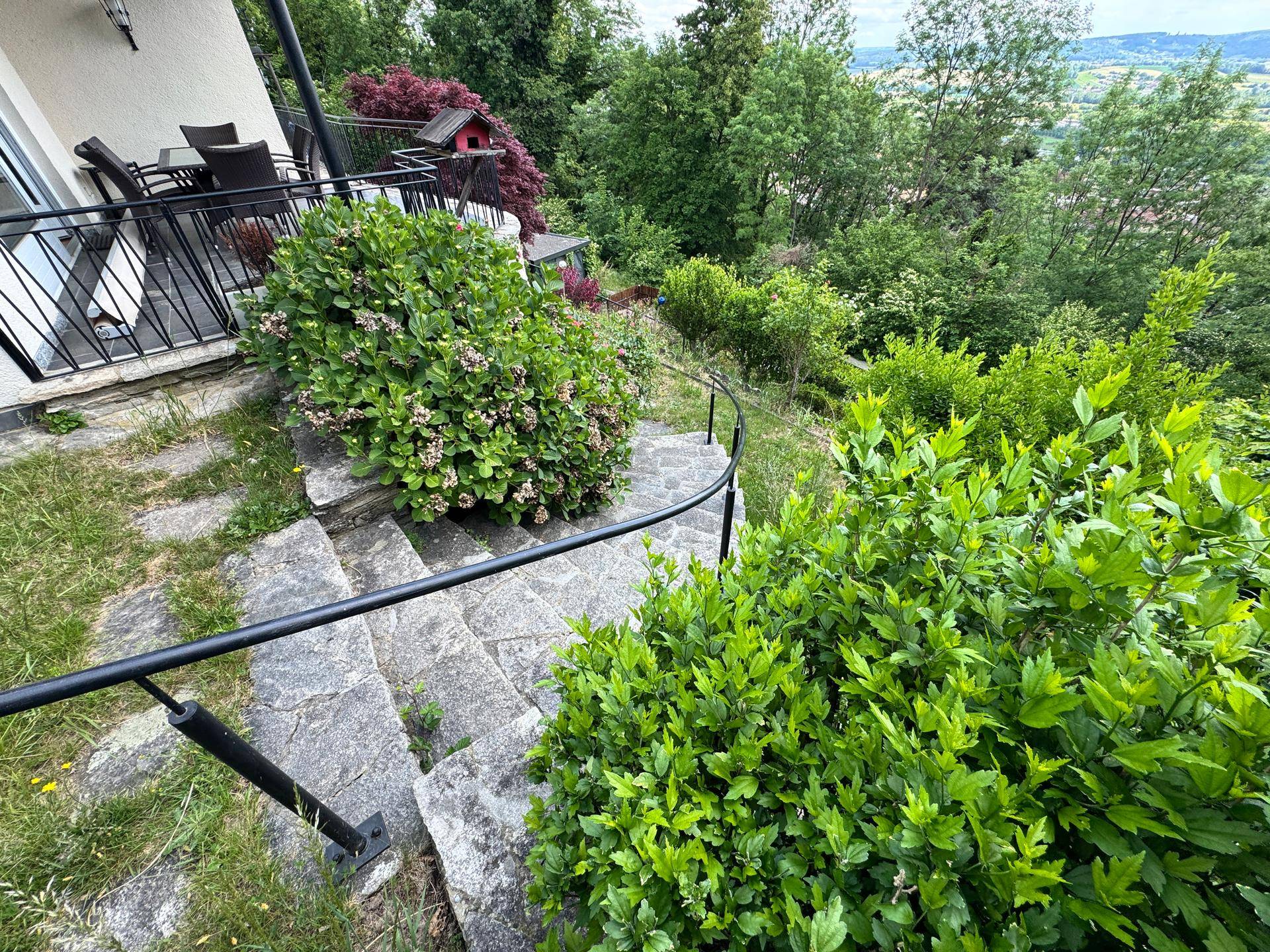 Geschwungene Steinstufen führen durch dichte Büsche bergauf, Teil des terrassierten Gartens.