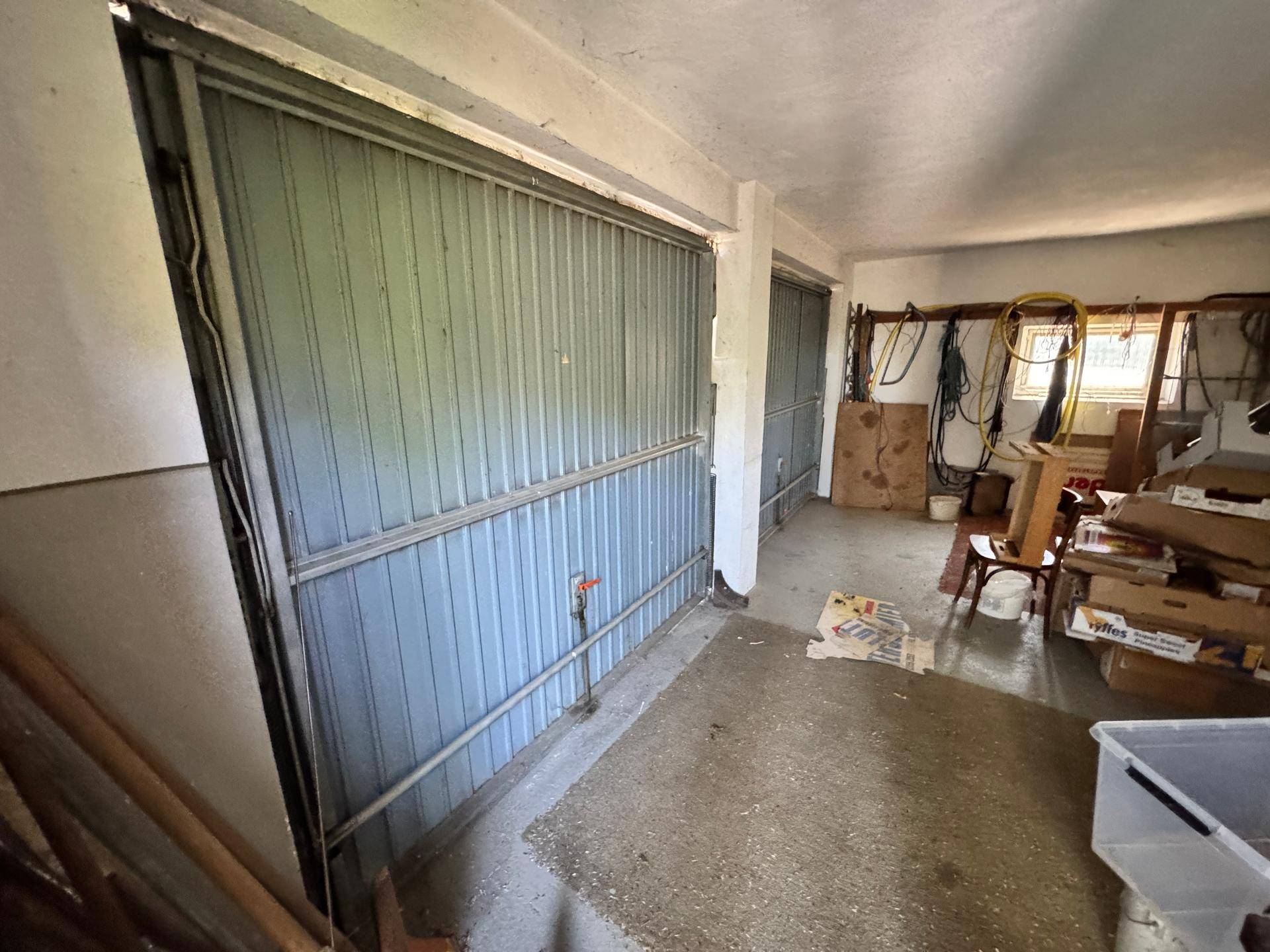 Geräumige Garage mit zwei Metalltoren und verschiedenen gelagerten Gegenständen.