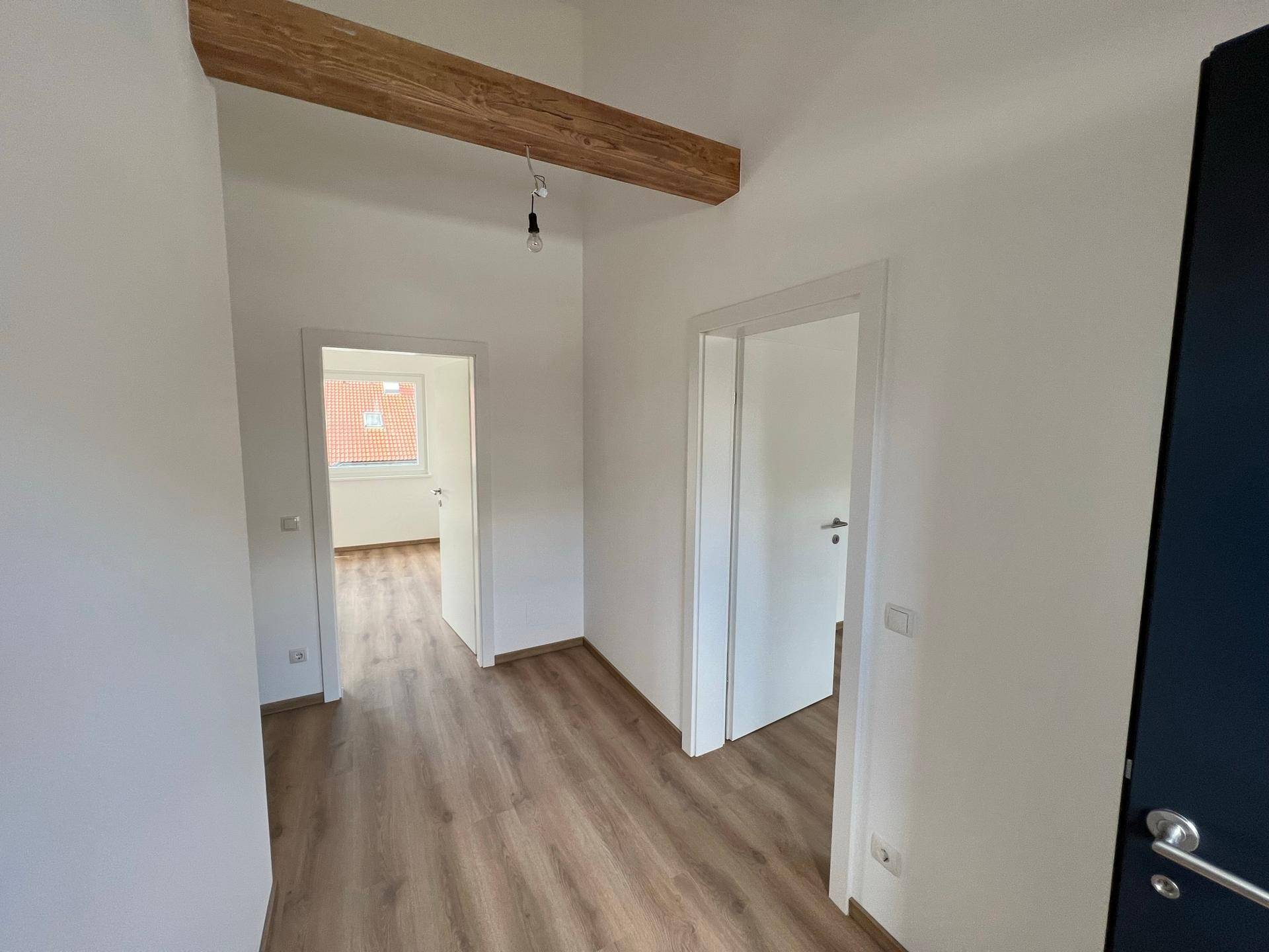Heller Flur mit Laminatboden und sichtbarem Holzbalken, der zu weiteren Räumen führt.