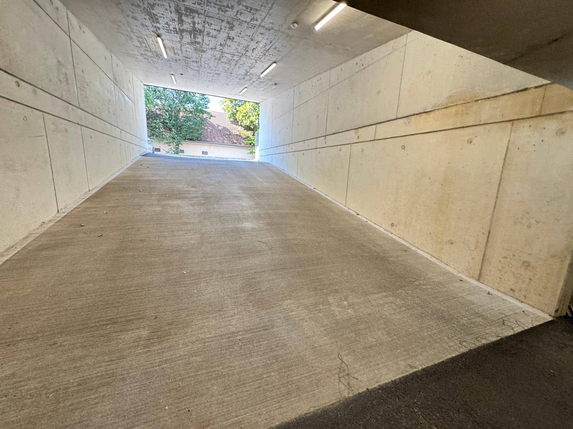 Ausfahrt einer Tiefgarage mit Betonrampe und Blick auf die grüne Umgebung.