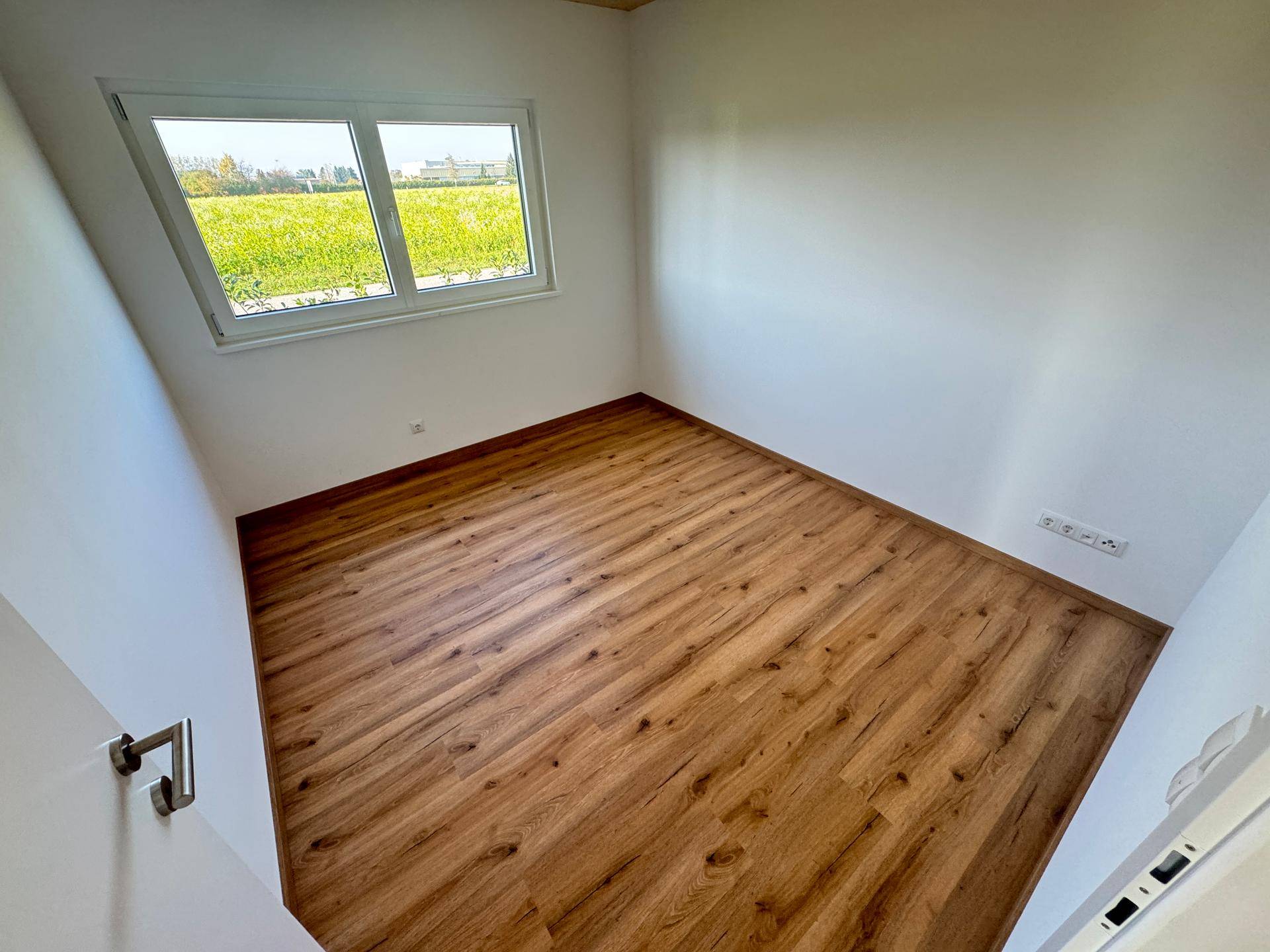 Helles Schlafzimmer mit Laminatboden und großem Fenster mit Blick auf die Landschaft.
