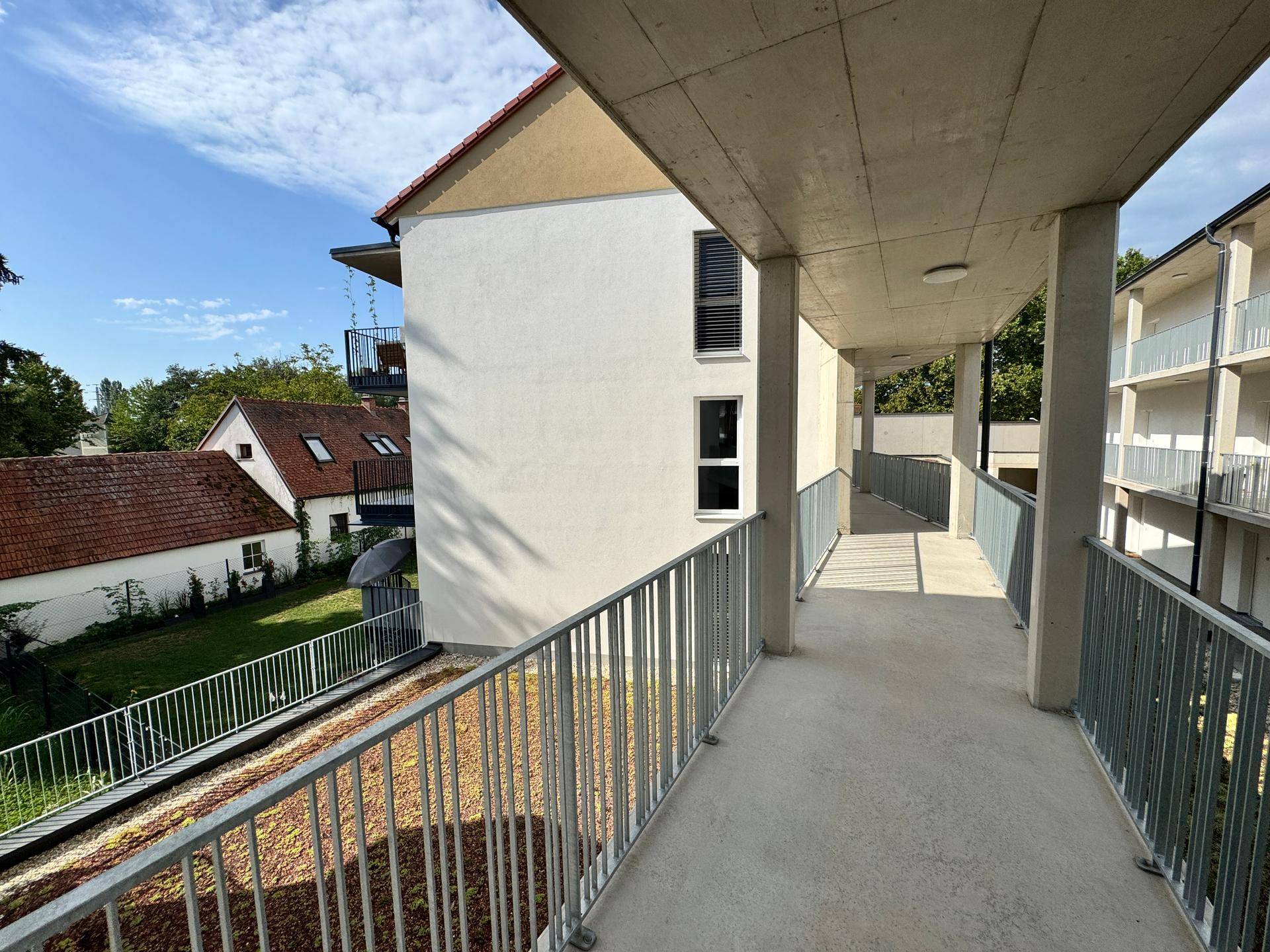 Offener Laubengang im Obergeschoss eines modernen Wohngebäudes mit Blick auf Nachbarhäuser.
