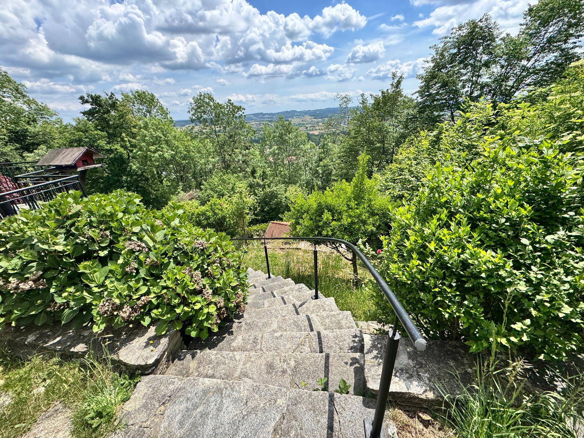 Steinstufen führen durch üppiges Grün bergauf, mit einem weiten Blick über die Landschaft.