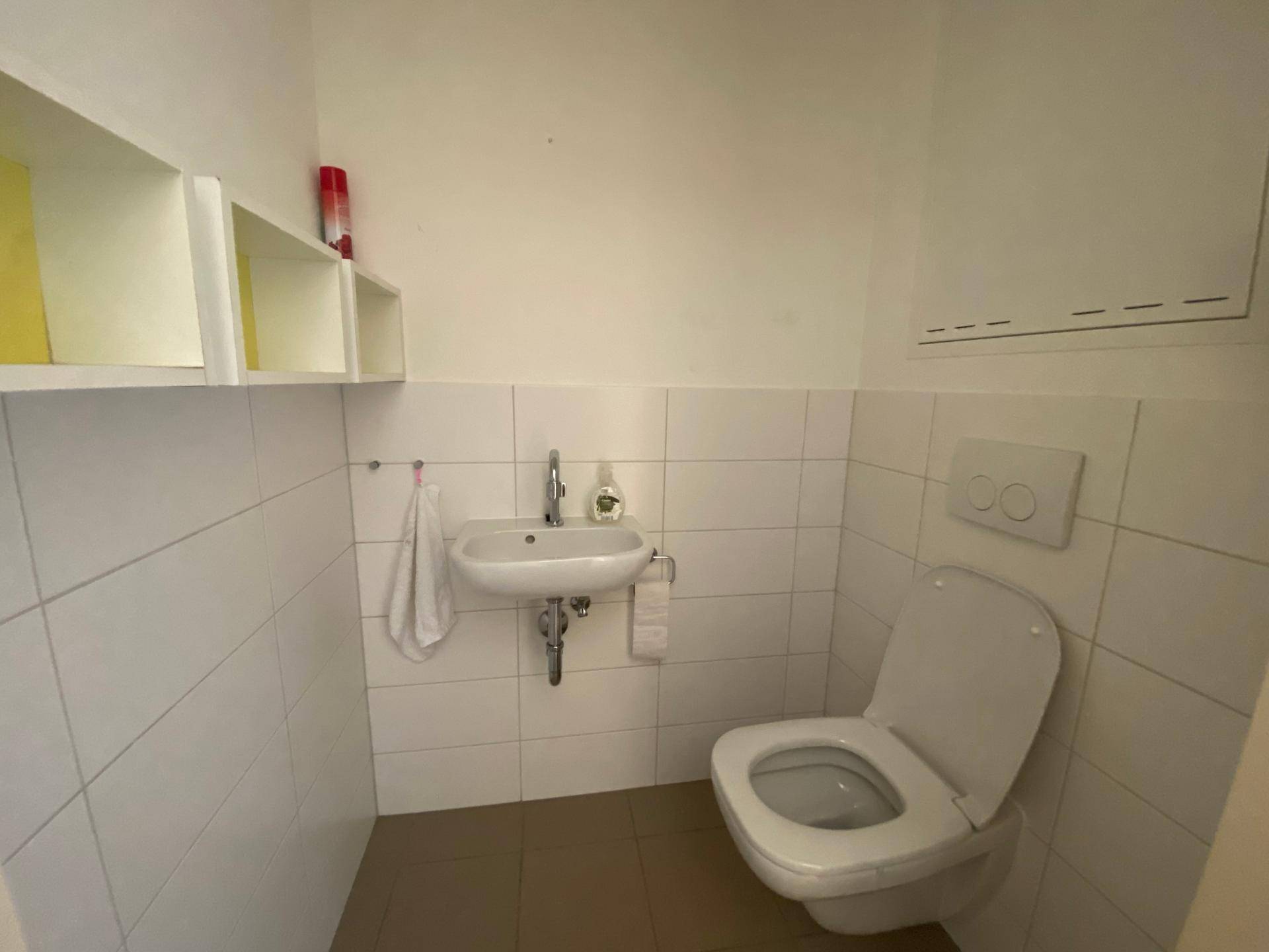 Kleines Gäste-WC mit weißen Fliesen, Toilette und Handwaschbecken.