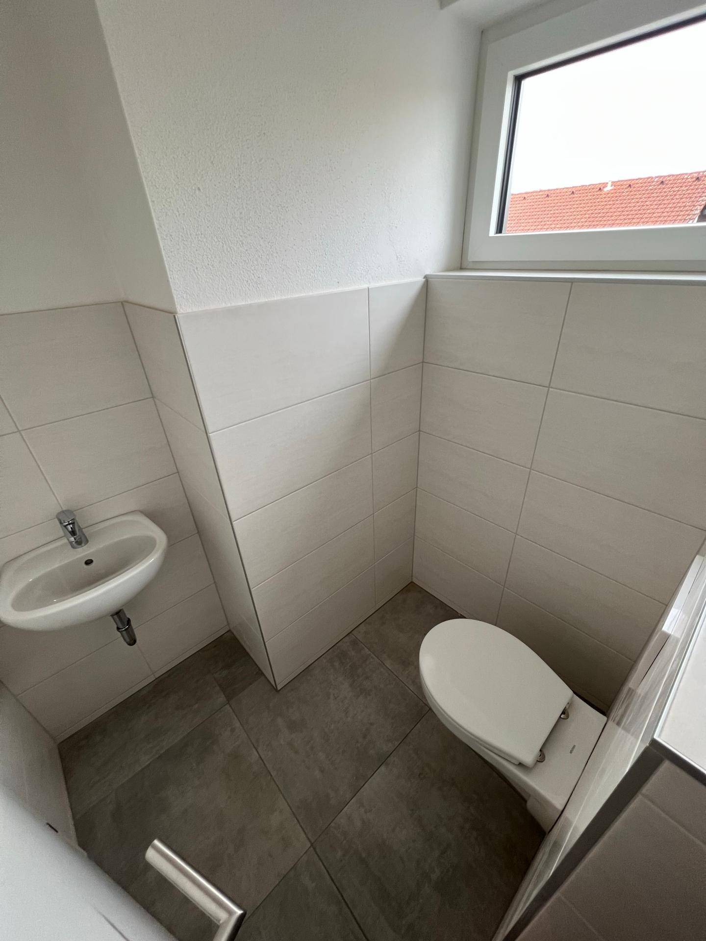 Modernes Gäste-WC mit hellen Fliesen, wandhängendem WC und kleinem Waschbecken.