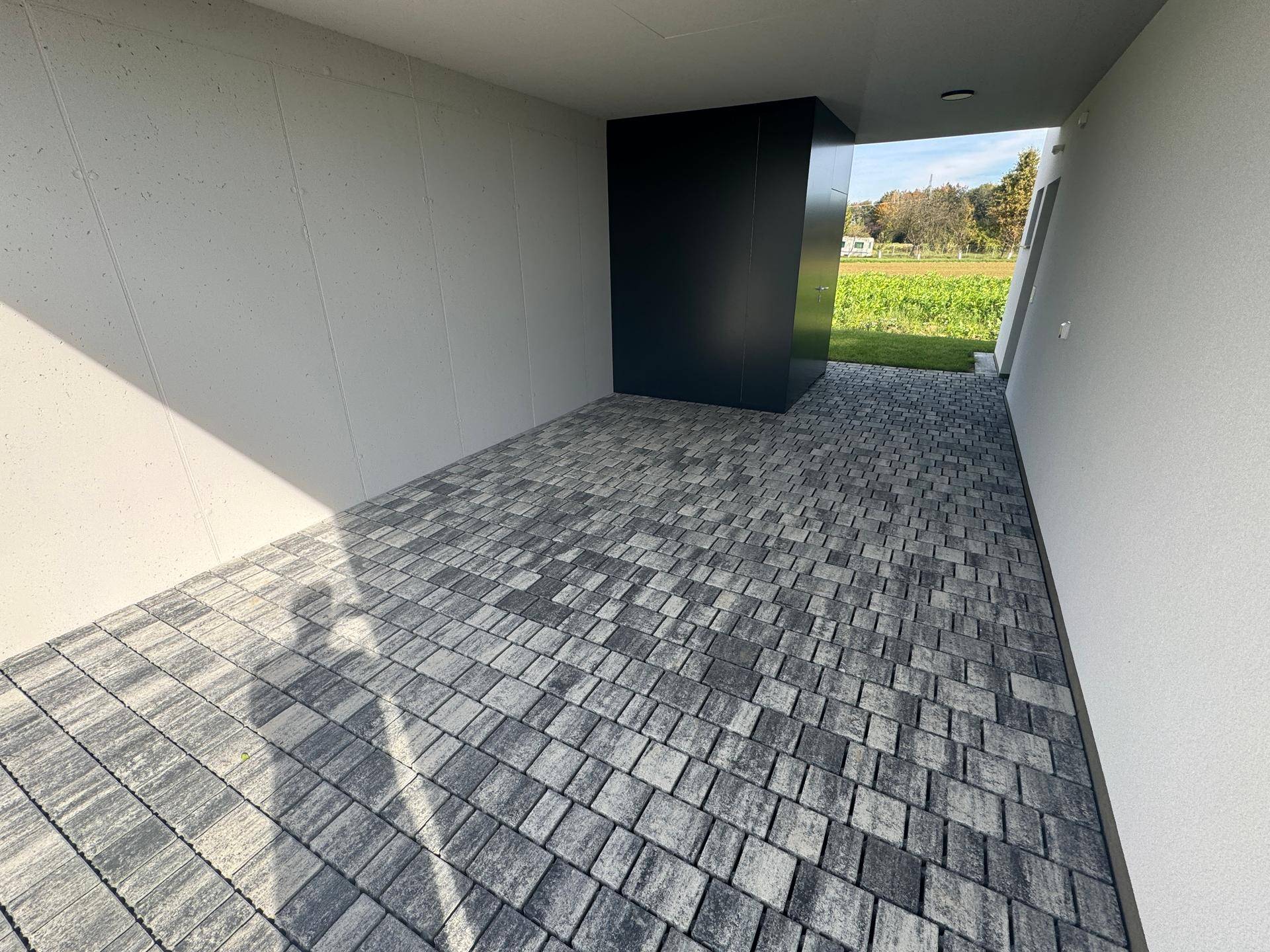 Geräumiger Carport mit gepflastertem Boden und Blick auf die umliegenden Felder.