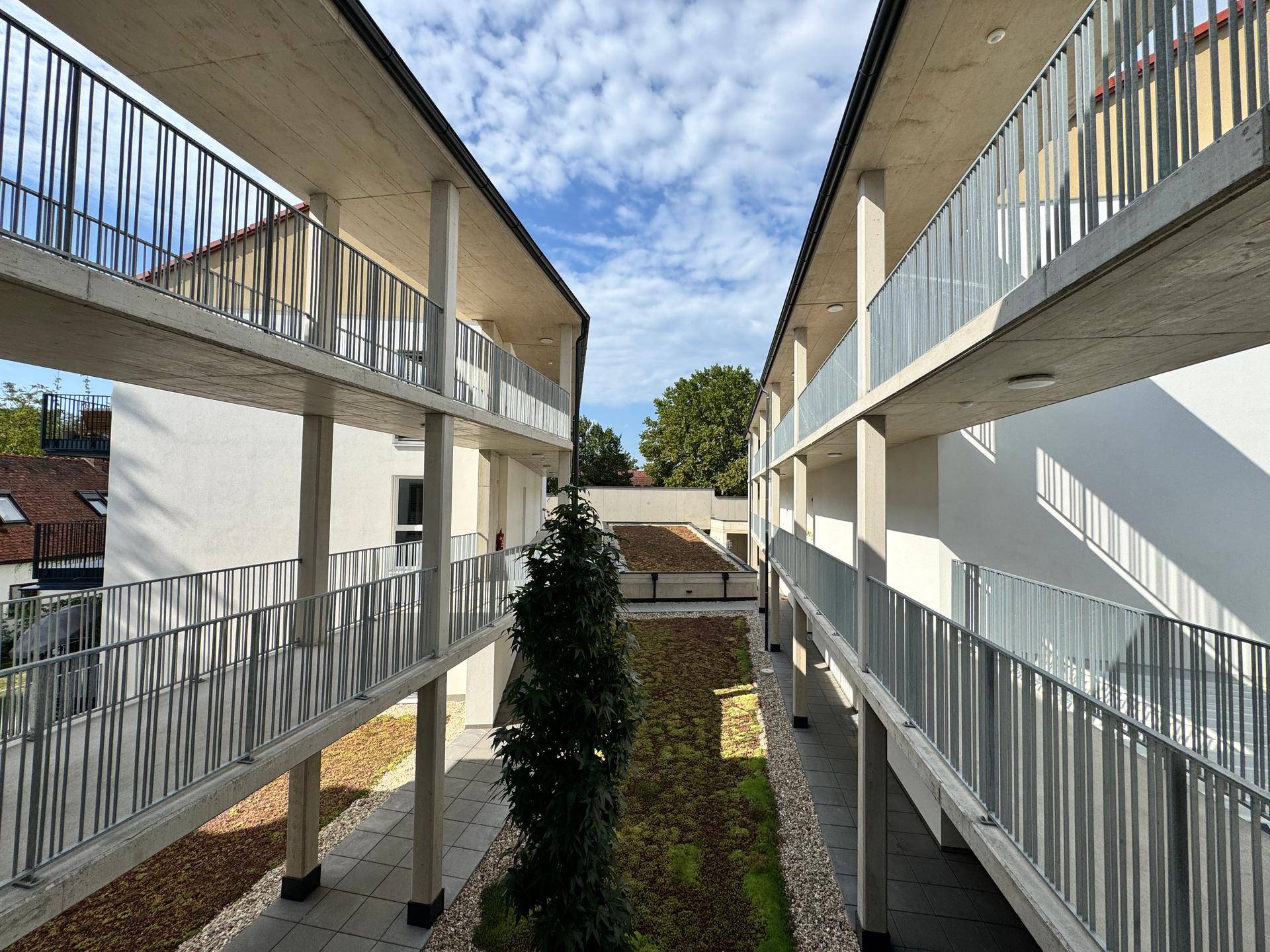 Ansicht des modernen Gebäudekomplexes mit mehreren Etagen und begrüntem Innenbereich.