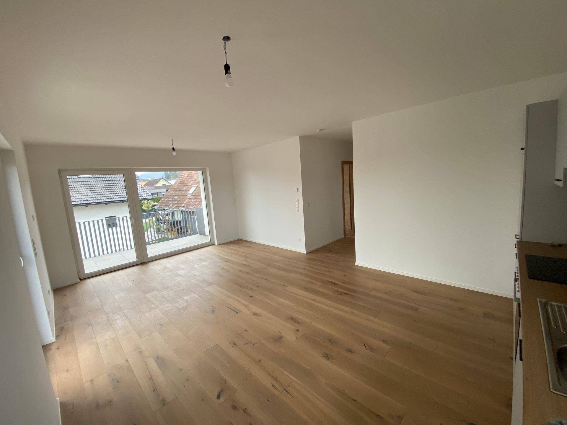 Heller Wohnbereich mit Holzboden und Zugang zu einem Balkon, der viel Tageslicht hereinlässt.