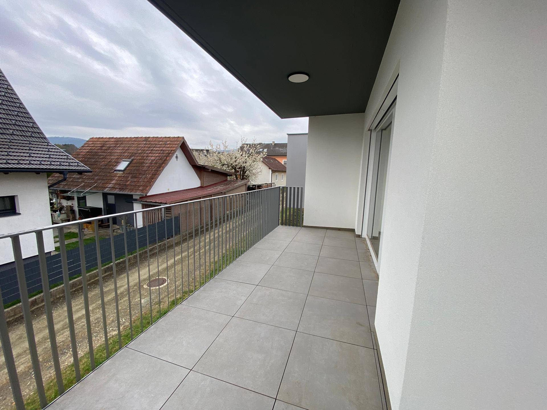 Geräumiger Balkon mit modernen grauen Fliesen und Metallgeländer, bietet Blick auf die Nachbarschaft.