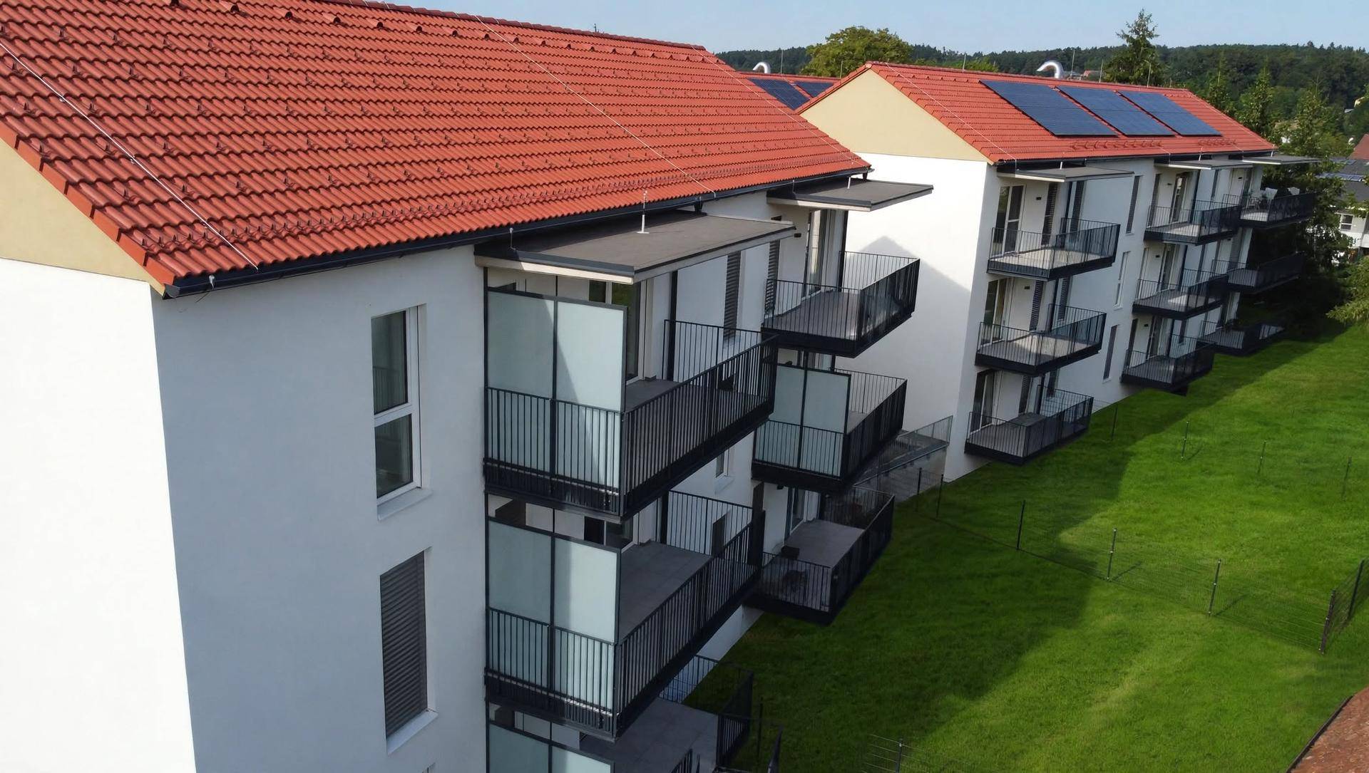 Seitenansicht eines modernen Wohngebäudes mit weißen Fassaden, zahlreichen Balkonen und grüner Umgebung.