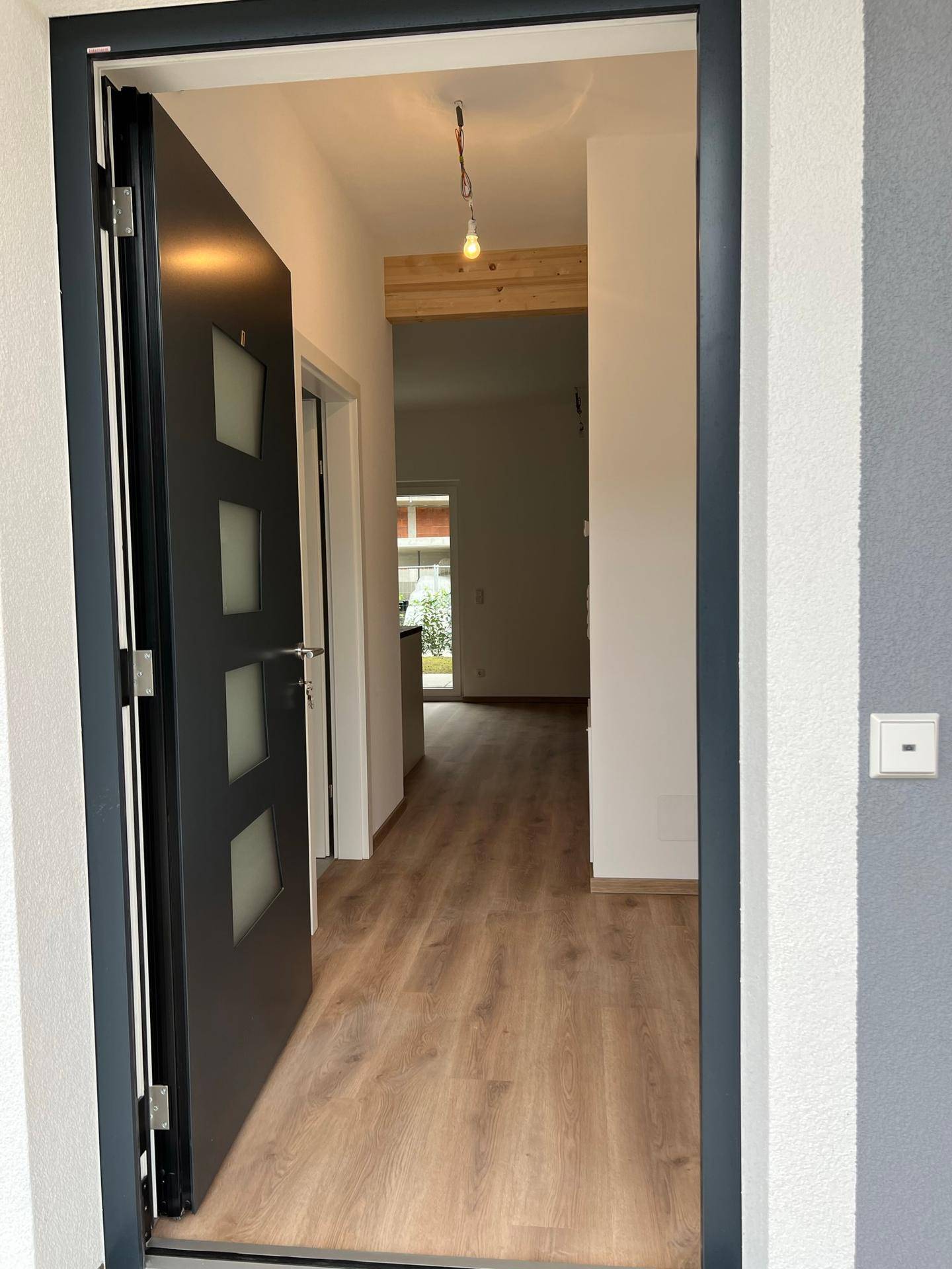 Heller Eingangsbereich mit moderner dunkler Tür, hellem Laminatboden und einem sichtbaren Holzbalken.