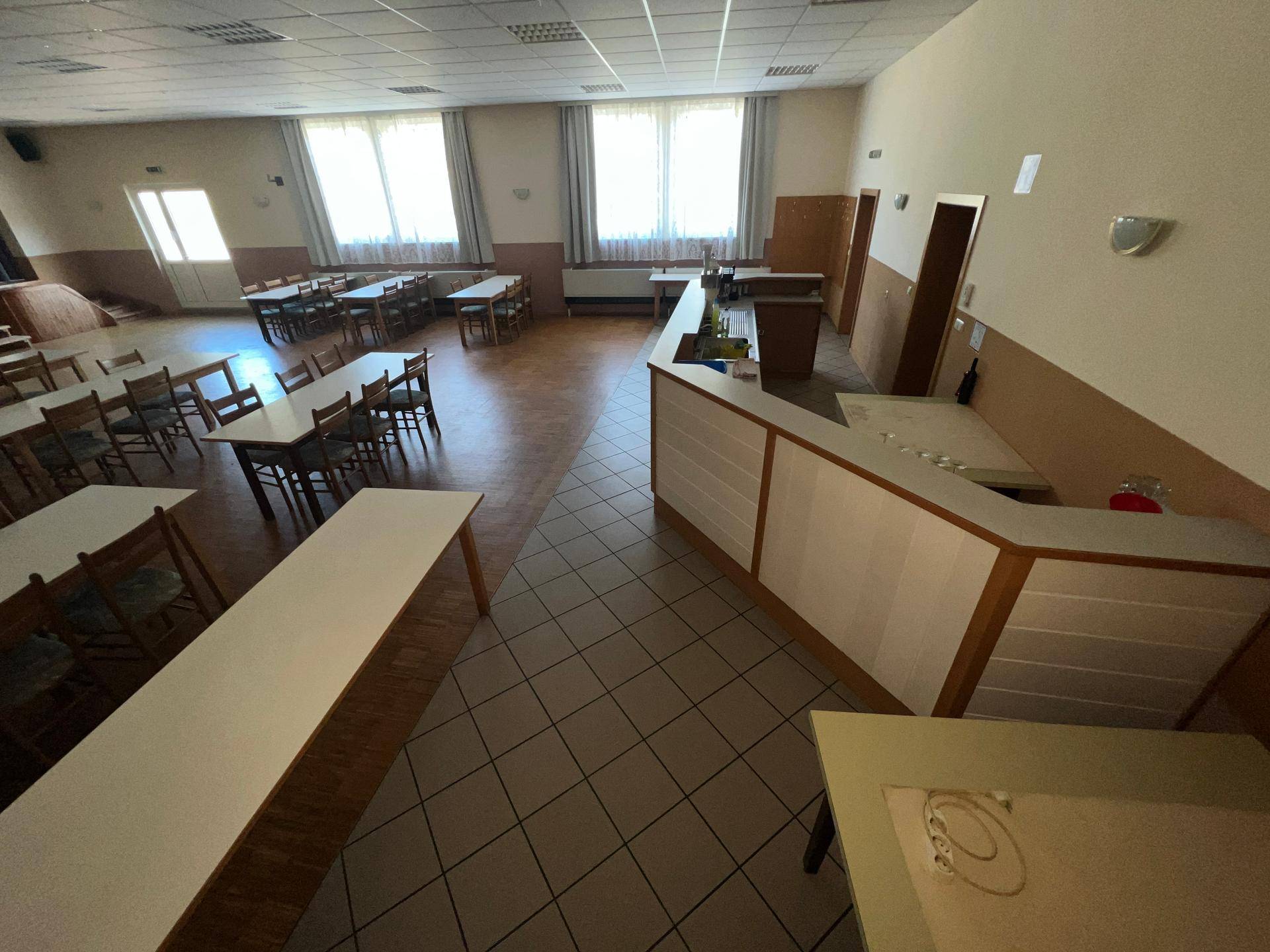 Geräumiger Speisesaal mit Tischen, Stühlen und einer Theke, bereit für Gäste.