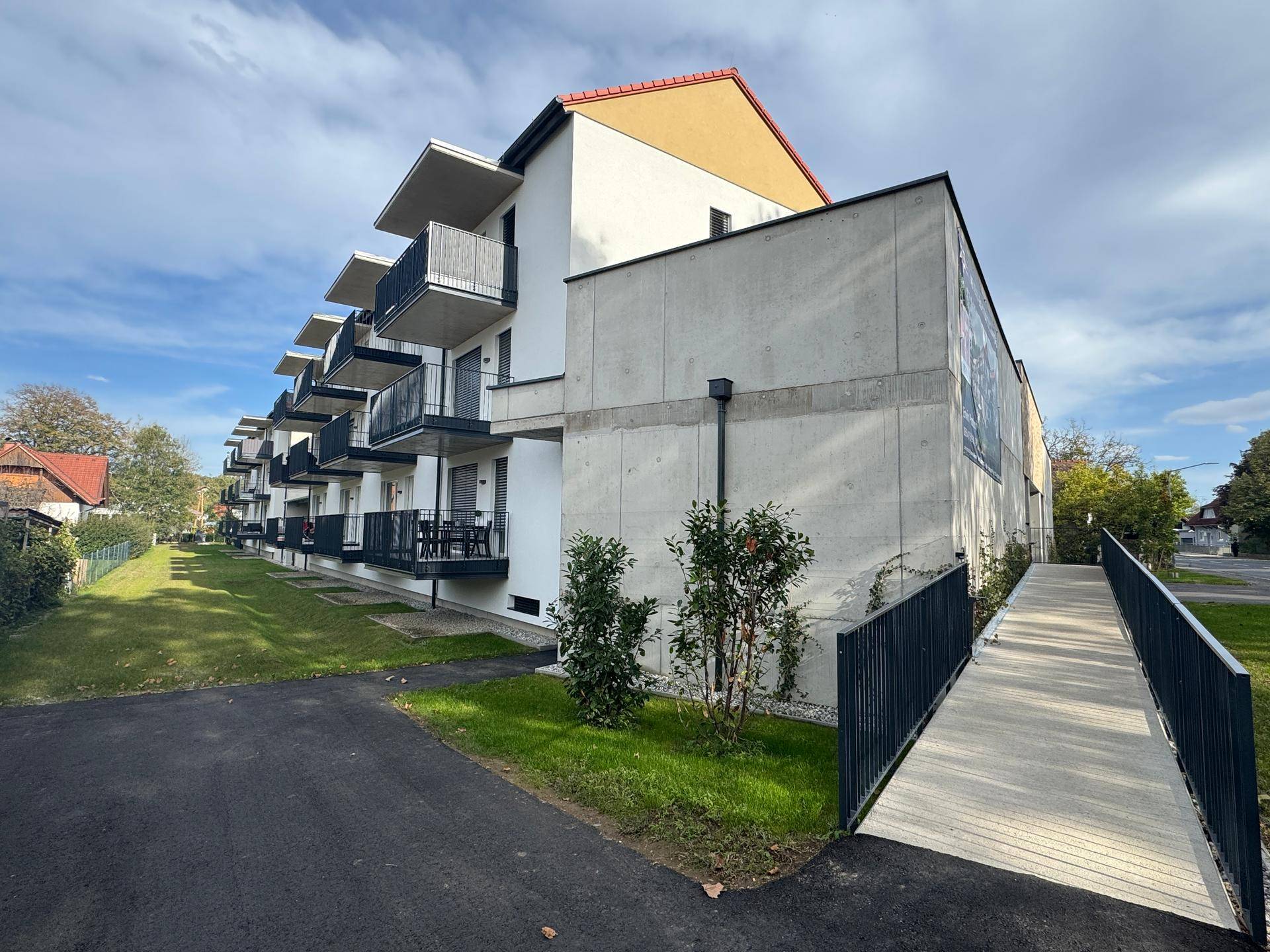 Moderne Gebäudefassade mit Rampe für barrierefreien Zugang und Grünfläche.