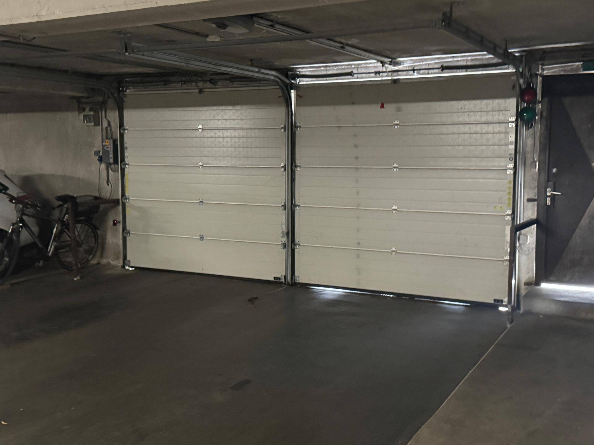 Zwei weiße Garagentore in einer Tiefgarage mit einem Fahrradabstellplatz daneben.