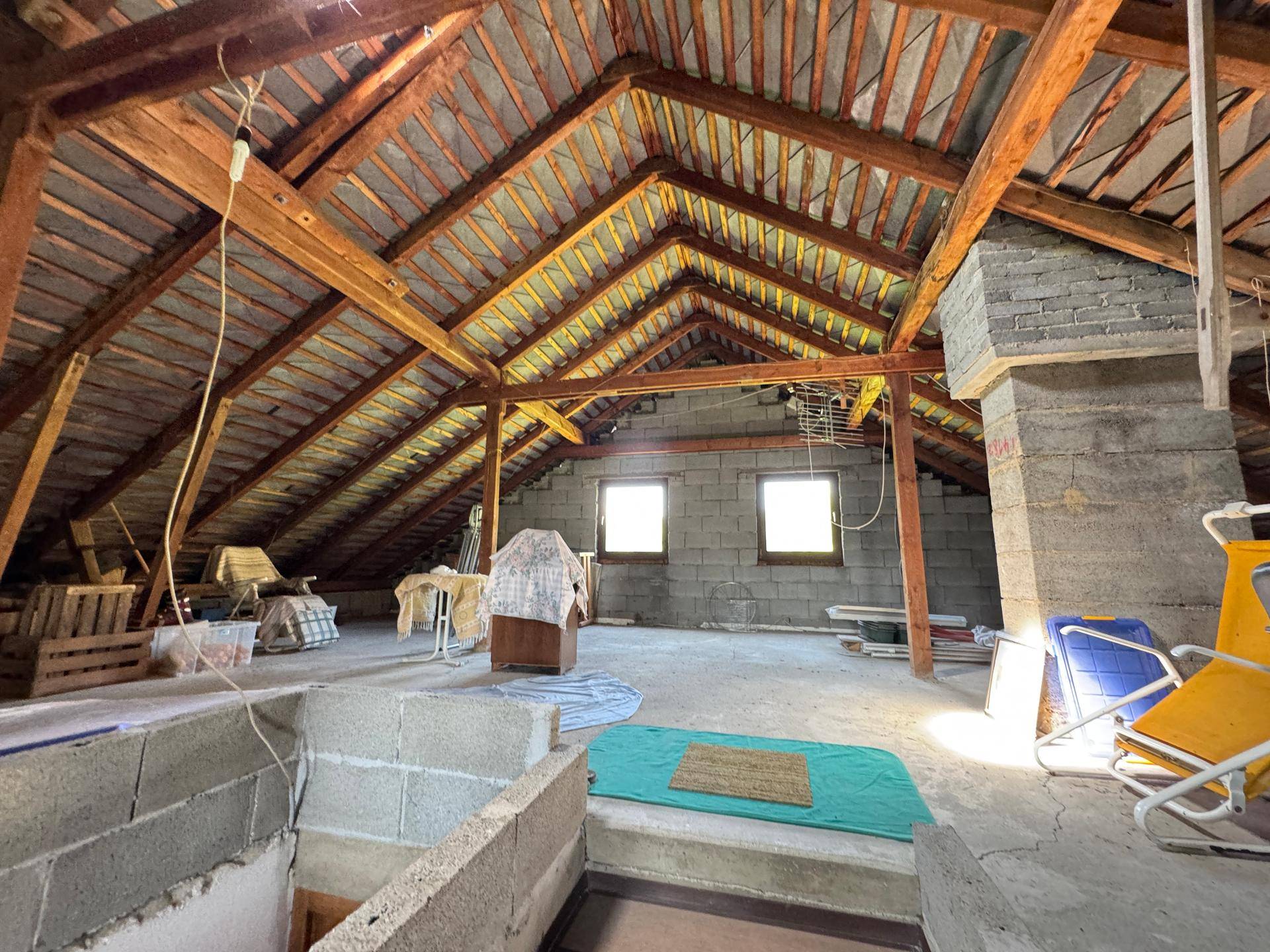 Geräumiger unausgebauter Dachboden mit sichtbaren Holzbalken, Fenstern und viel Potenzial.
