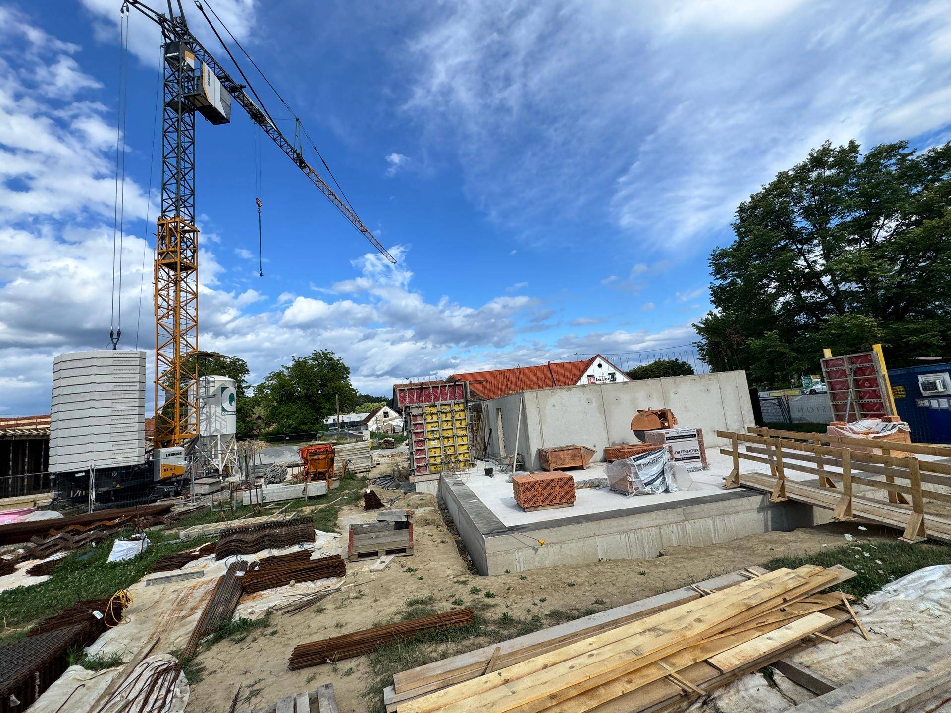 Baustelle mit Kran, Betonwänden und verschiedenen Baumaterialien unter einem dynamischen Wolkenhimmel.