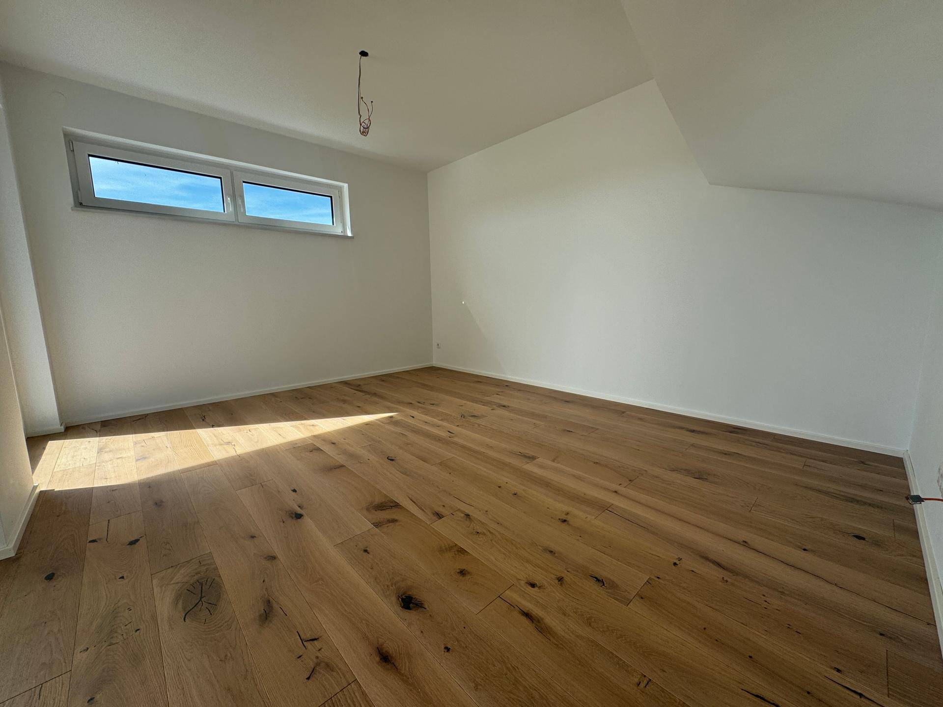 Helles Schlafzimmer mit Eichenparkett, weißen Wänden und Dachschräge.