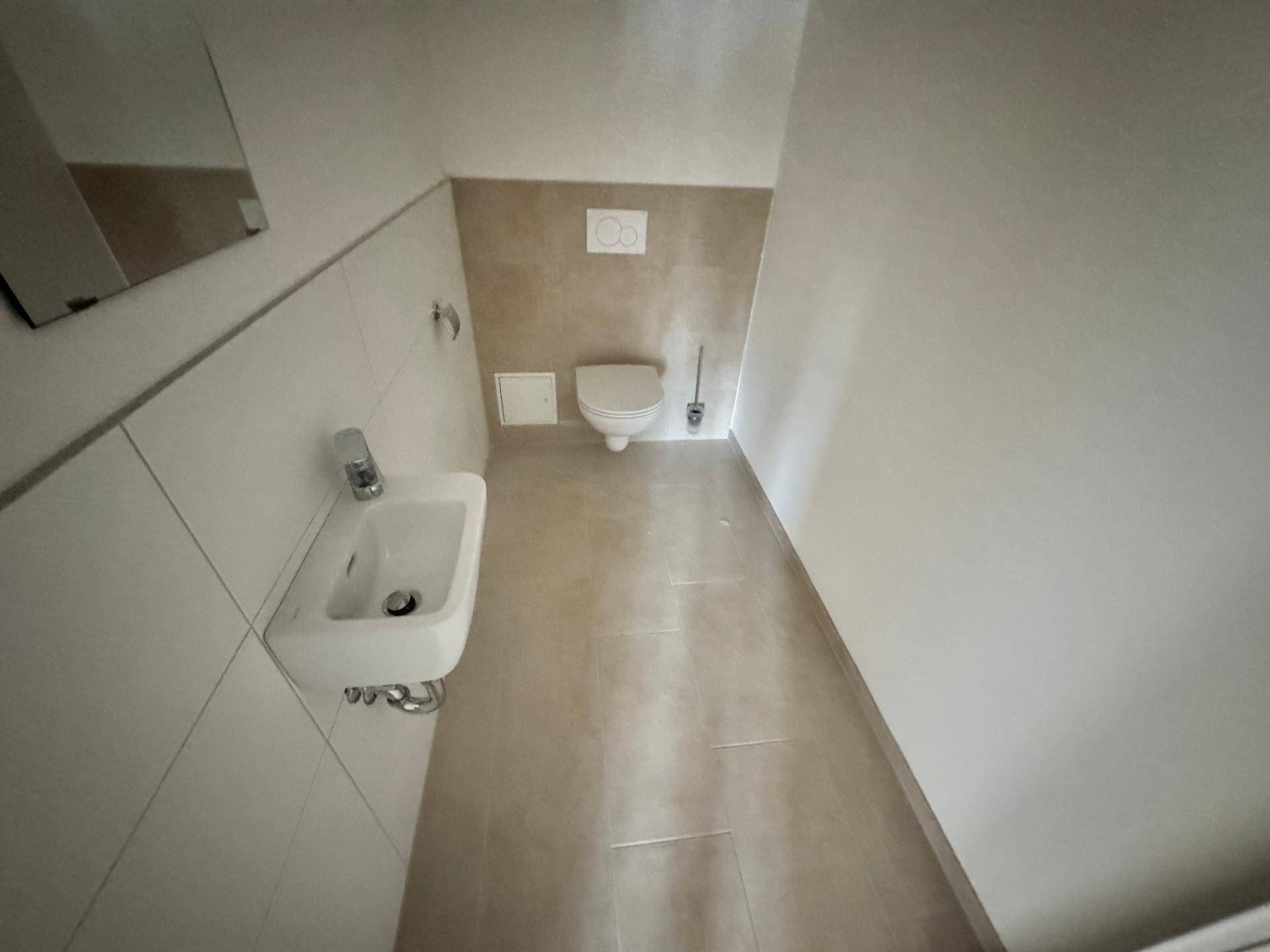 Kleines Gäste-WC mit Wand-WC, Waschbecken und beigefarbenen Wandfliesen.