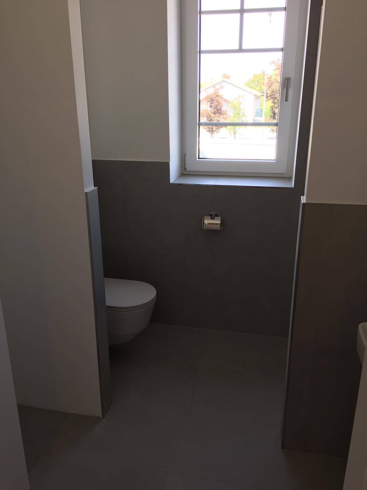Modernes Gäste-WC mit Wand-WC, grauen Fliesen und Fenster für Tageslicht.