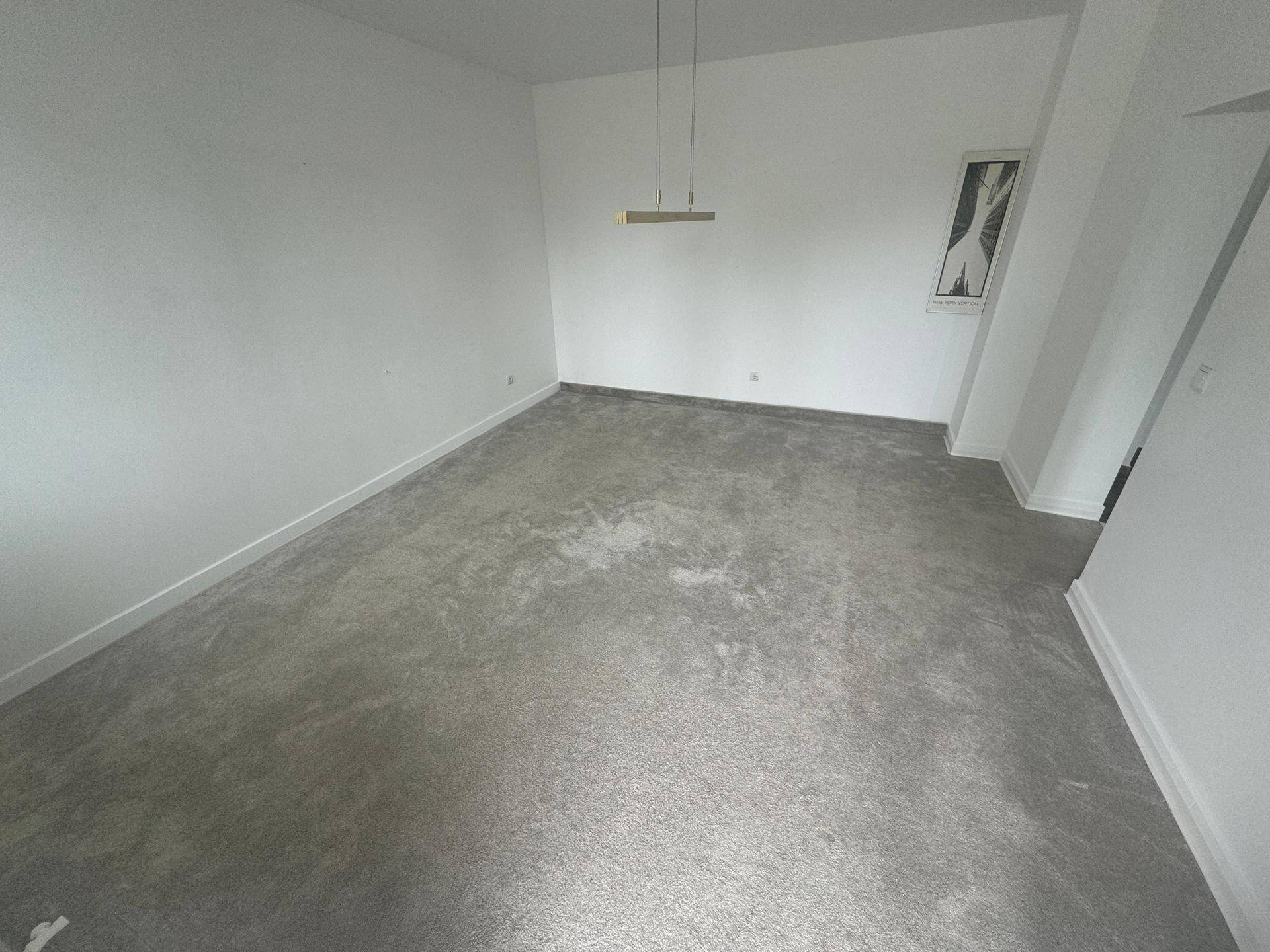 Geräumiger, heller Raum mit grauem Teppichboden und minimalistischer Deckenbeleuchtung, ideal für Wohnzwecke.