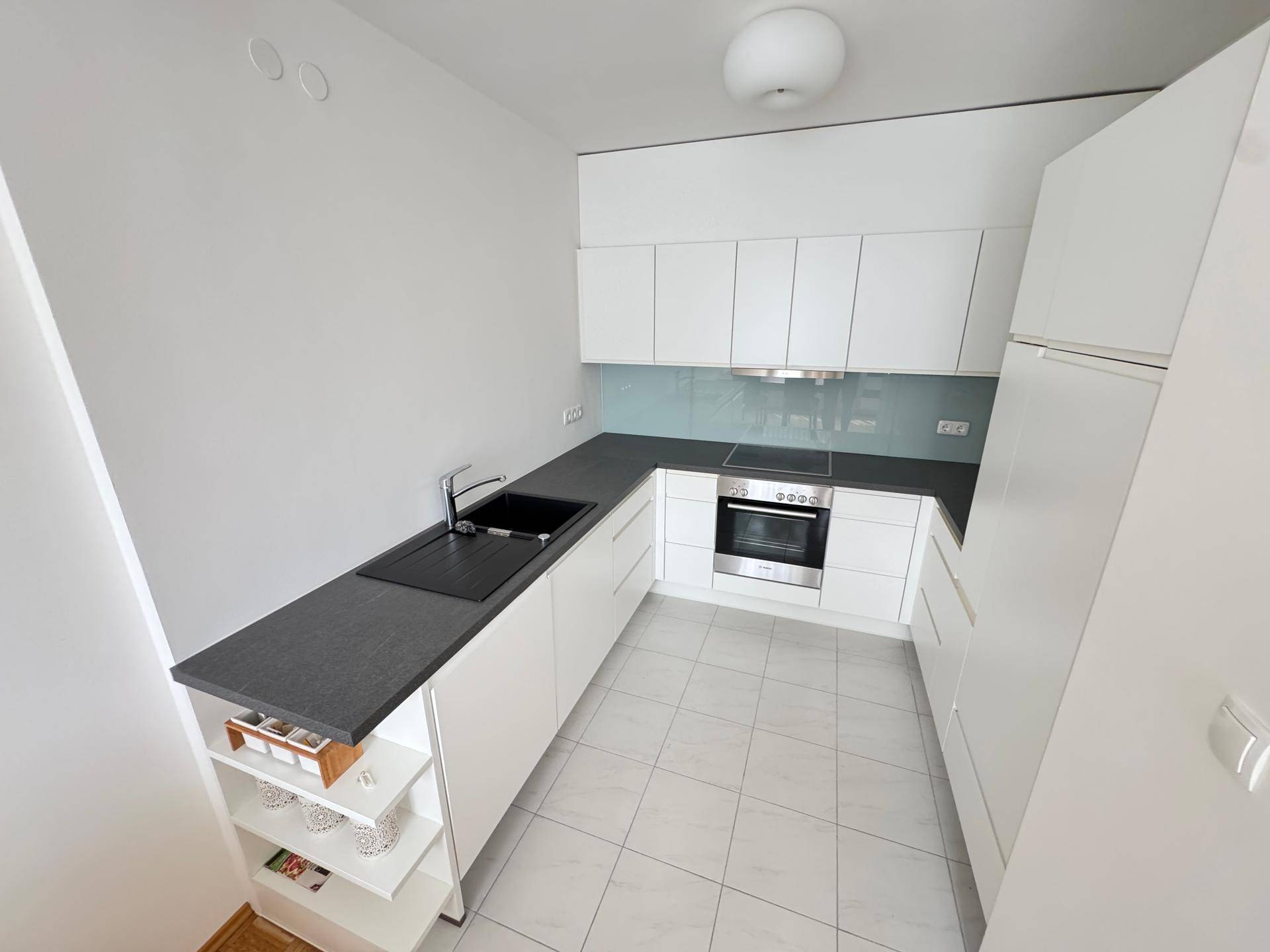 Moderne Einbauküche mit weißen Schränken, dunkler Arbeitsplatte und hellen Fliesenboden.