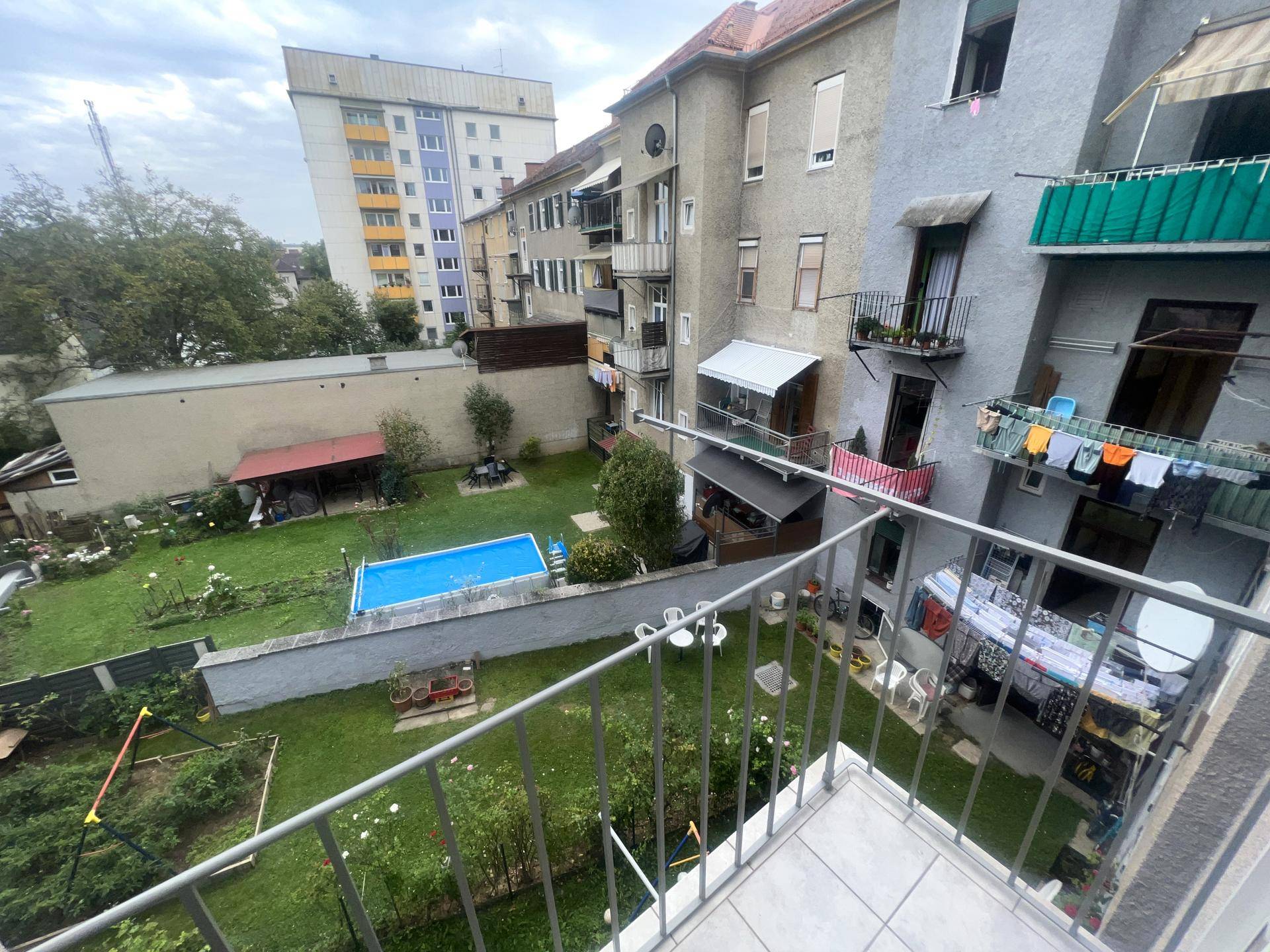 Balkon mit Blick auf einen Gemeinschaftsgarten mit Pool und Spielplatz.