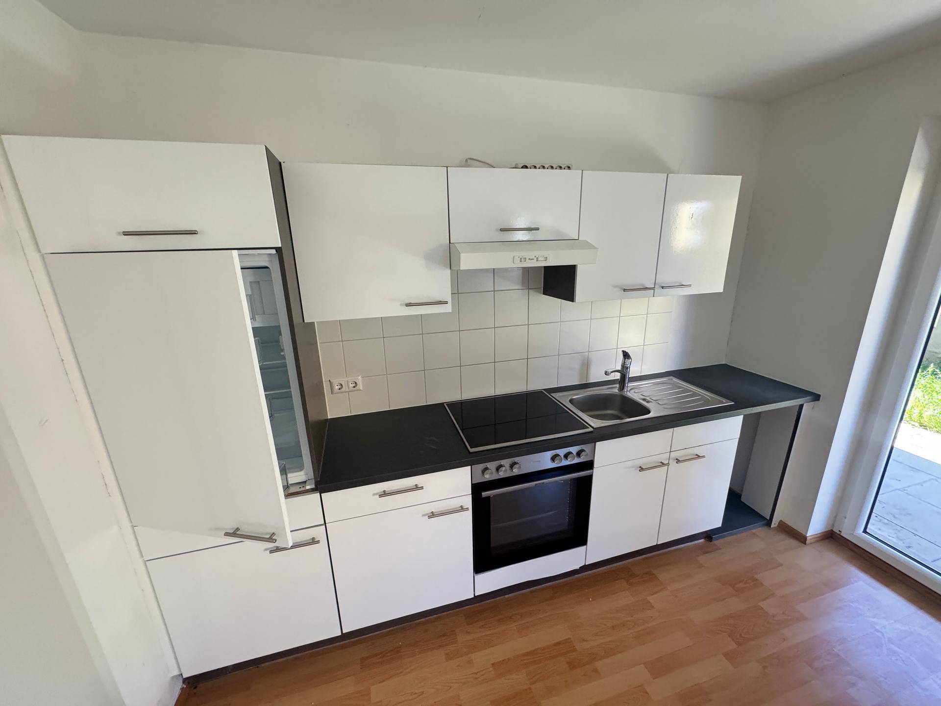 Moderne Einbauküche mit weißen Schränken, schwarzer Arbeitsplatte und integrierten Geräten.