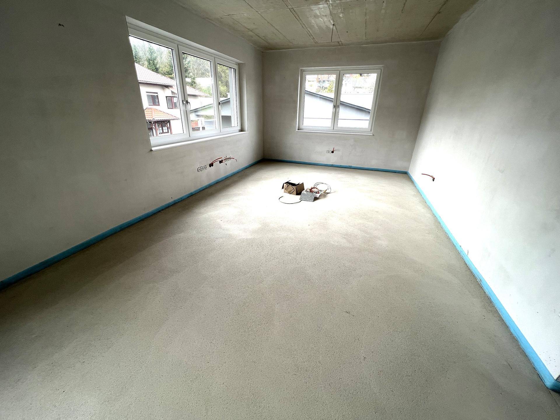 Leerer Büroraum im Rohbau mit Betonboden und Fenstern, bereit für den Innenausbau.