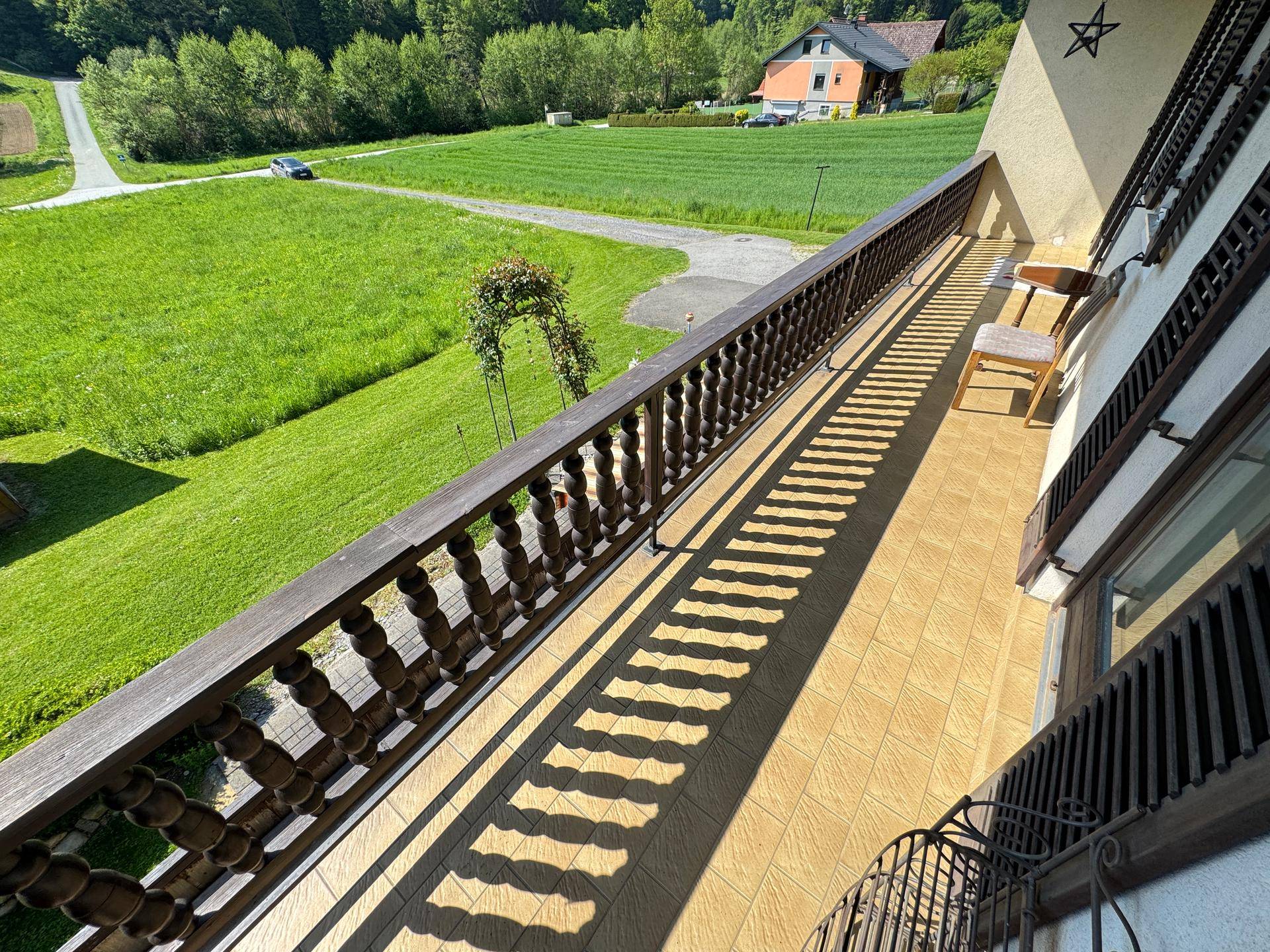Langer Balkon mit Holzgeländer und weitem Blick über grüne Felder und die Landschaft.