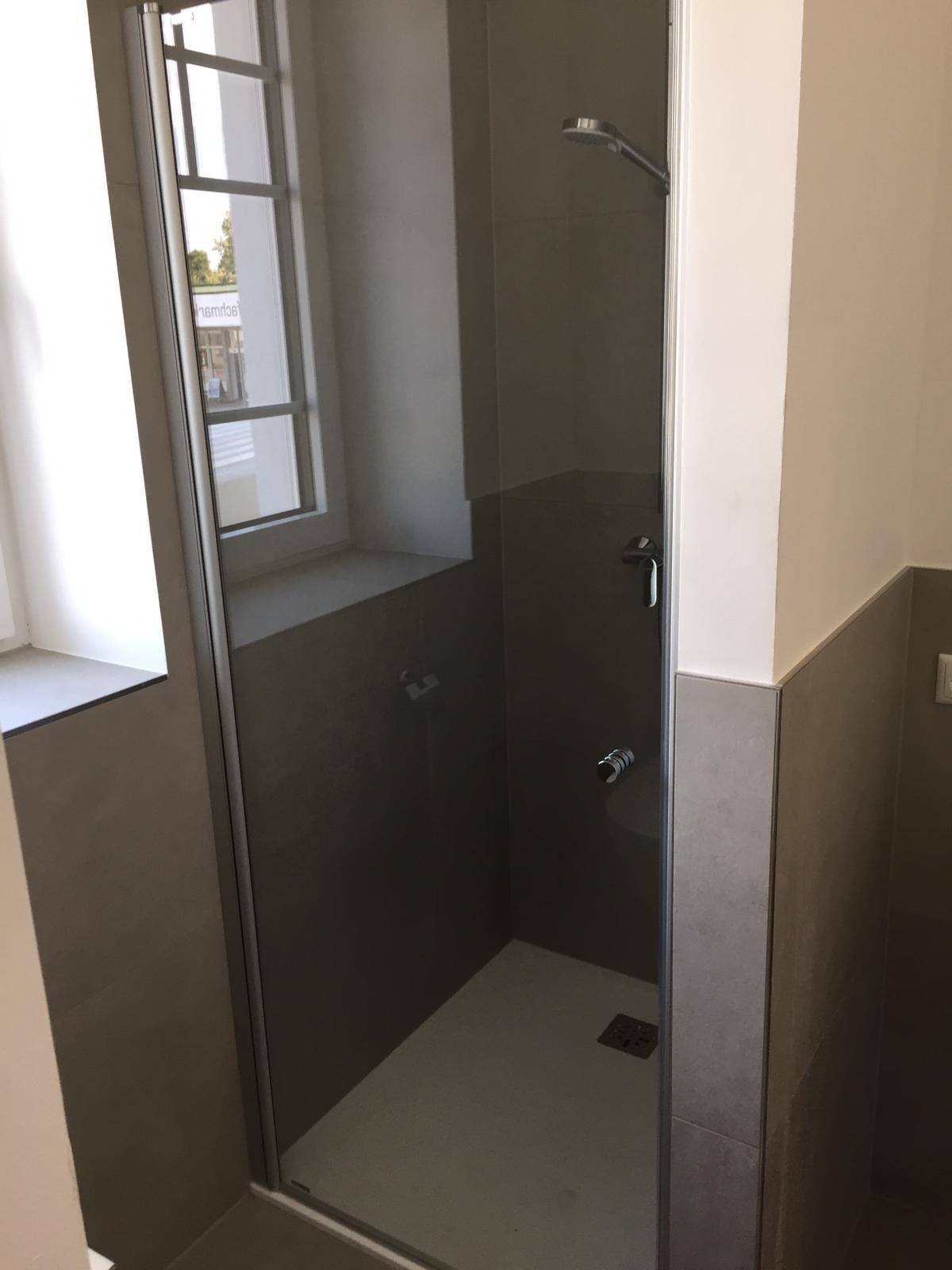 Moderne Duschkabine mit Glaswand und grauen Fliesen im Badezimmer.