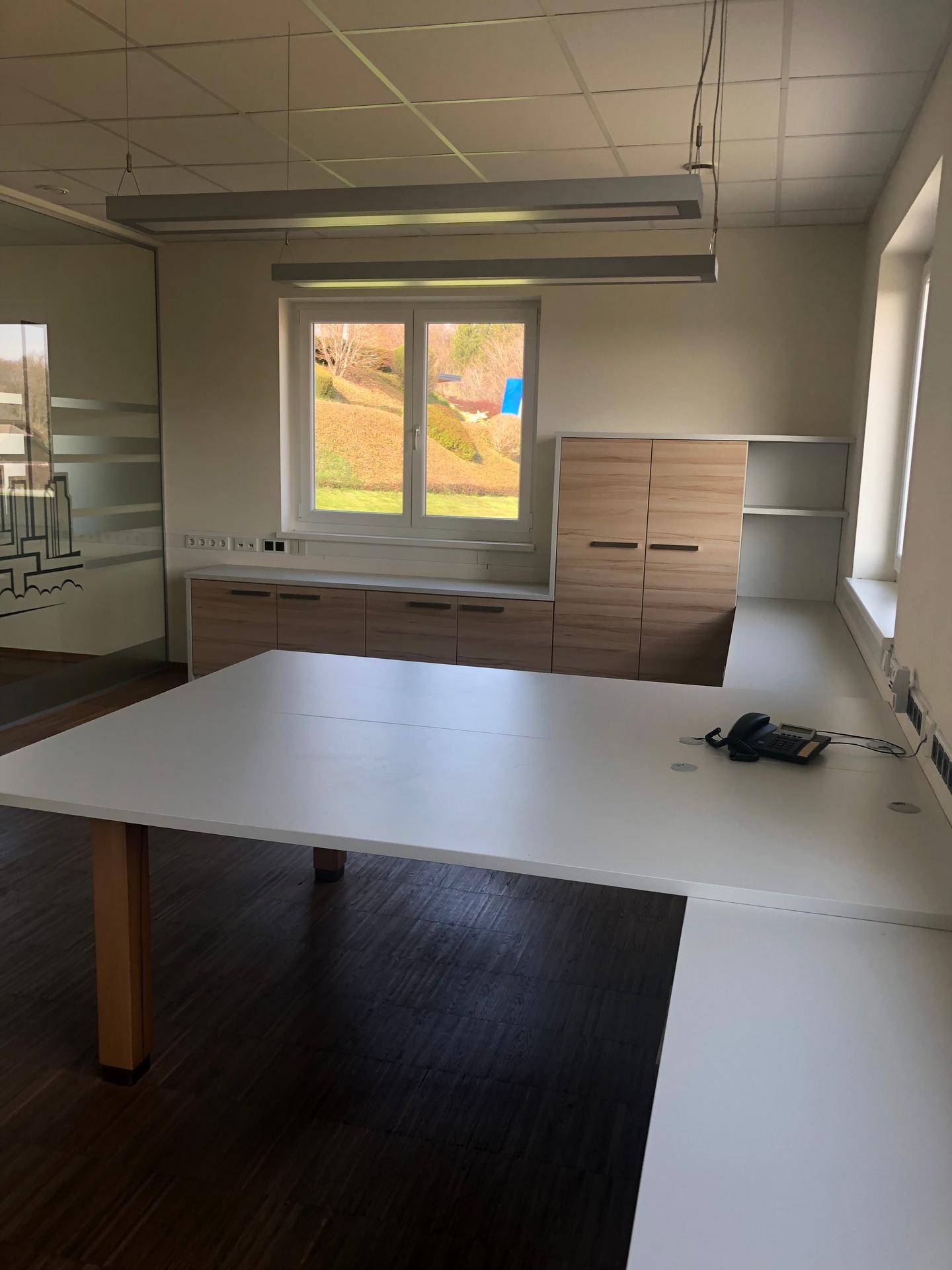 Helles Büro mit großem Schreibtisch, Holzschränken und Blick ins Grüne.