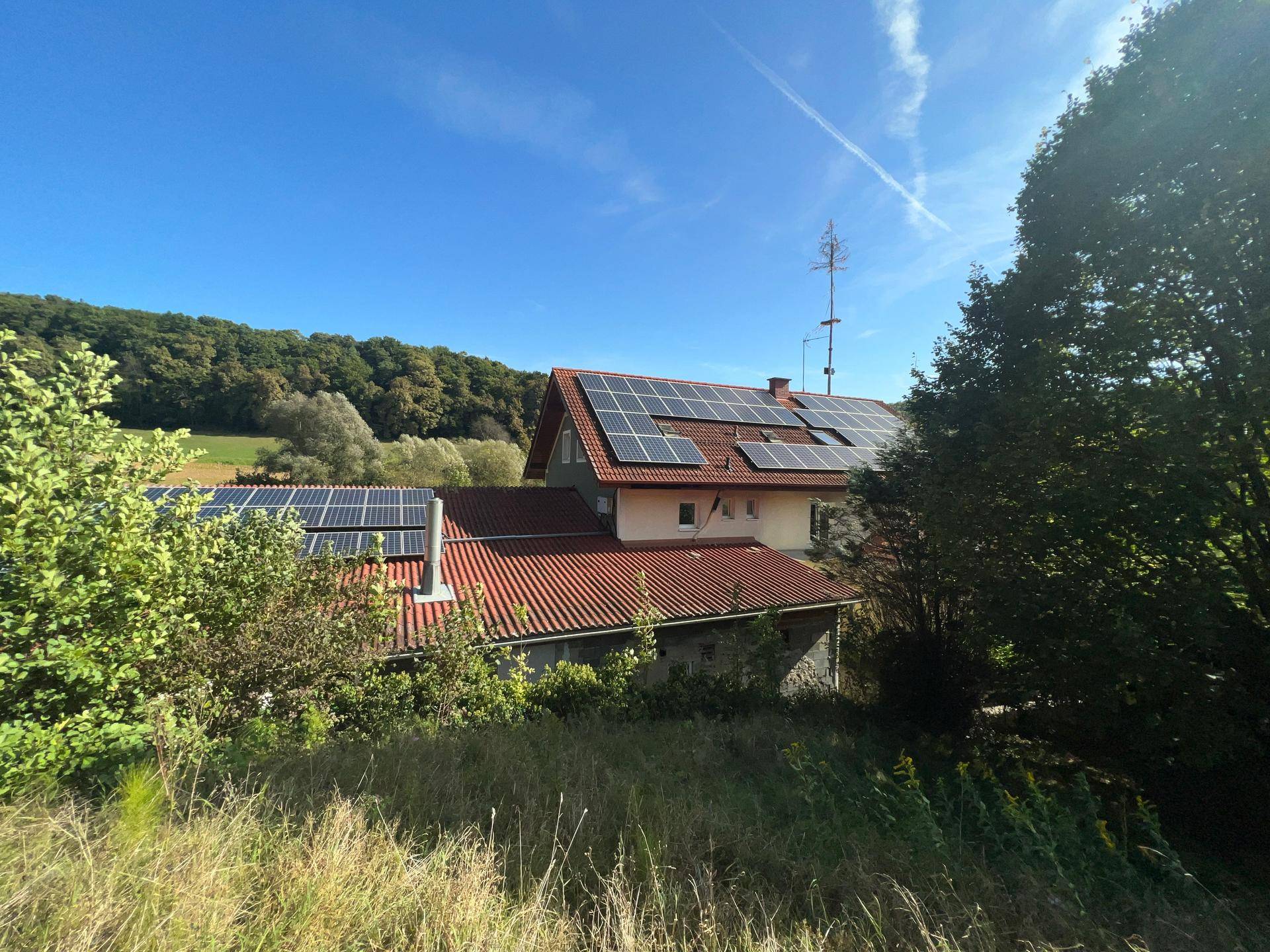 Dachansicht des Gebäudes mit zahlreichen Photovoltaik-Modulen und umgebender grüner Landschaft.