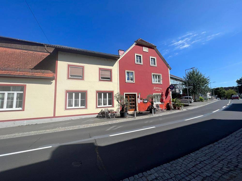 Gesamtansicht des Gebäudes von der Straße, mit roter und beiger Fassade und Außenbereich.