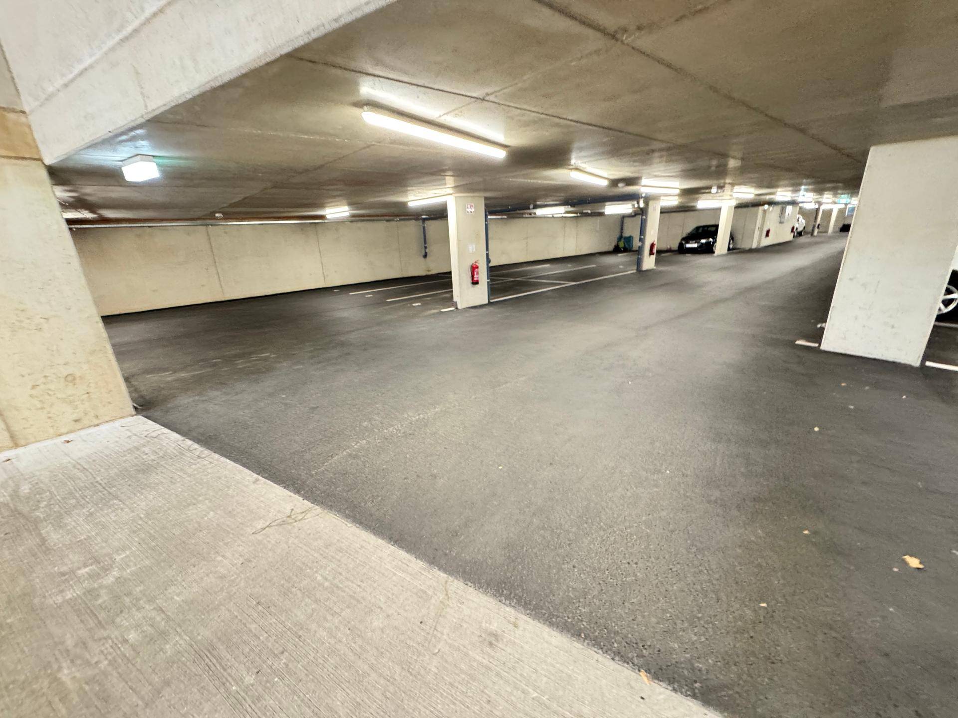 Geräumige Tiefgarage mit Betonstützen und markierten Parkplätzen, bietet sichere Abstellmöglichkeiten.