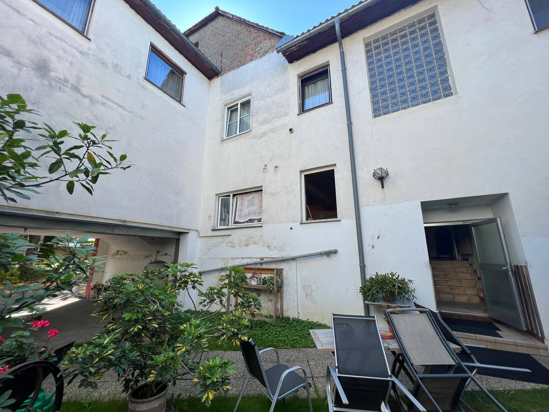 Kleiner Innenhof mit Pflanzen und Gartenmöbeln, umgeben von Gebäudewänden.