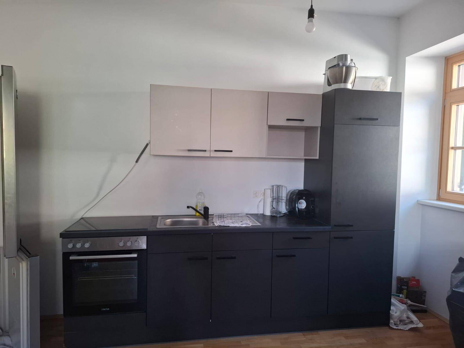 Funktionale Küche mit dunklen Schränken, integrierten Geräten und Fenster für Tageslicht.