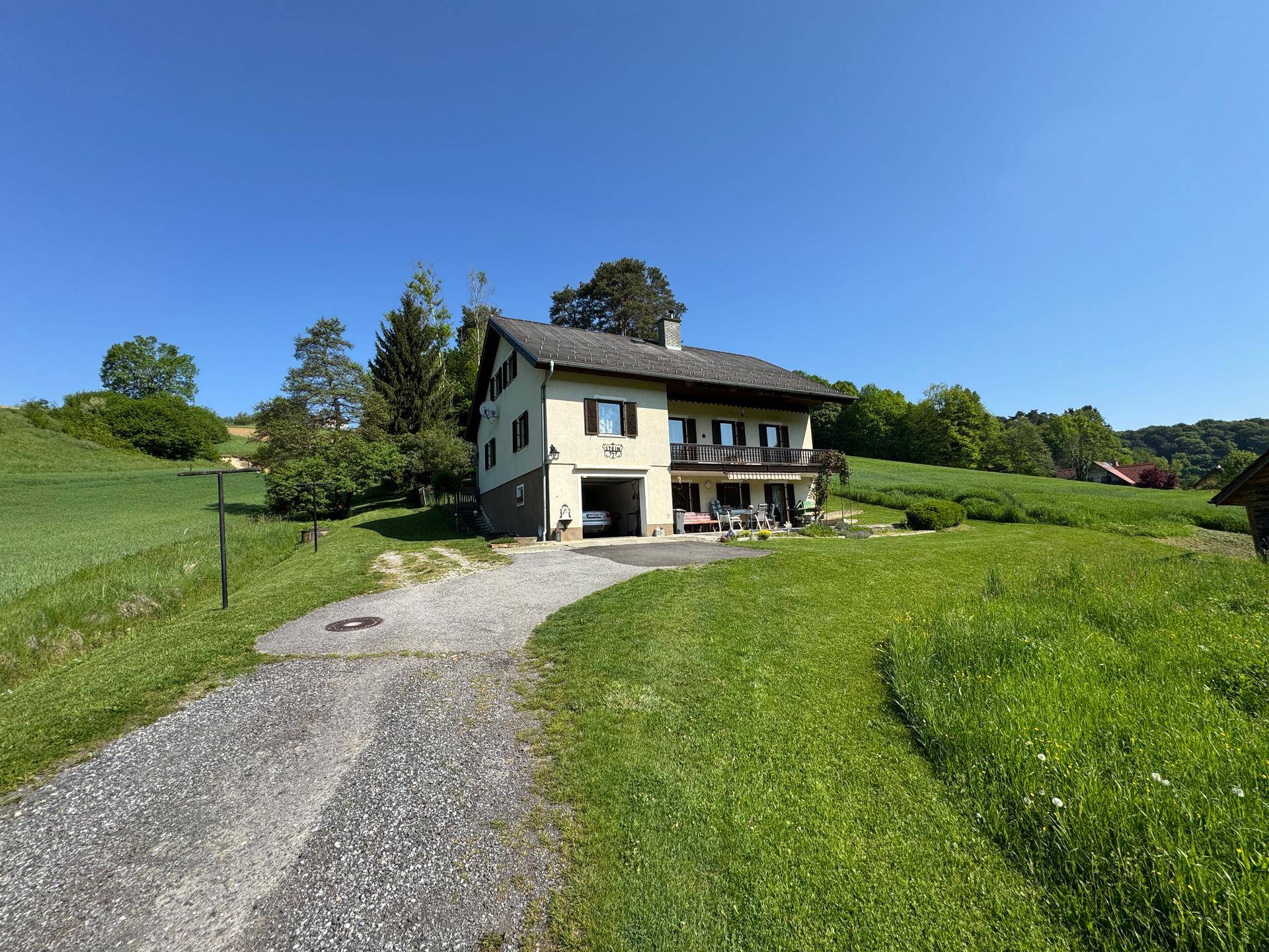 Freistehendes Haus mit Balkon und Garage, umgeben von weitläufigen grünen Wiesen.