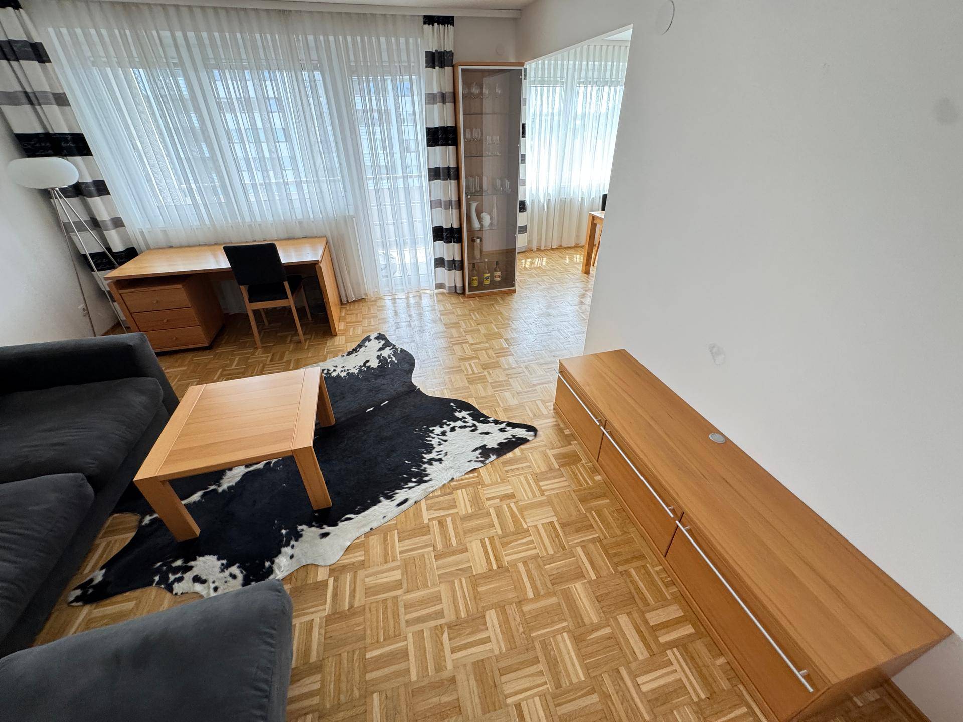 Geräumiges Wohnzimmer mit Parkettboden, bequemer Couch und Arbeitsbereich am Fenster.