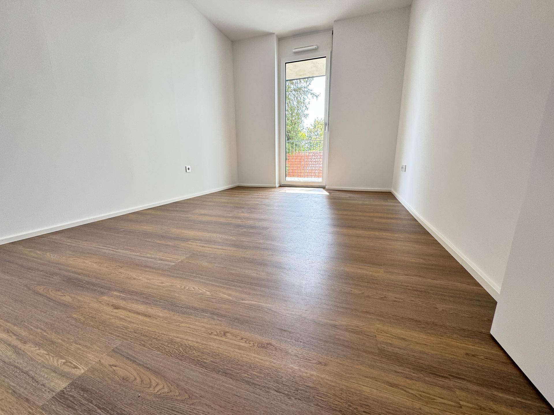 Geräumiges Schlafzimmer mit Laminatboden und Zugang zu einem Balkon oder einer Terrasse.