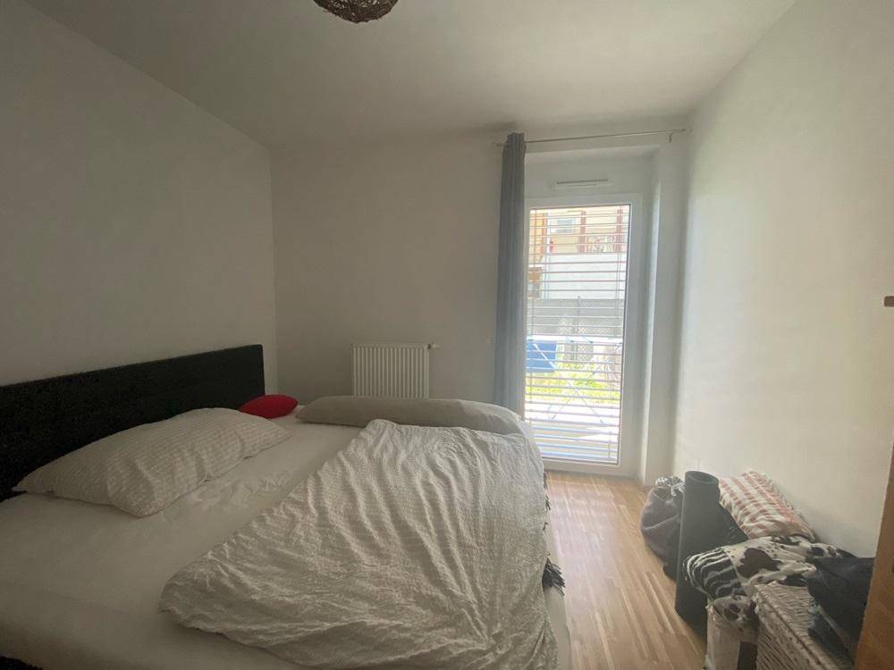 Schlafzimmer mit Holzboden, Doppelbett und Fenster mit Jalousien.